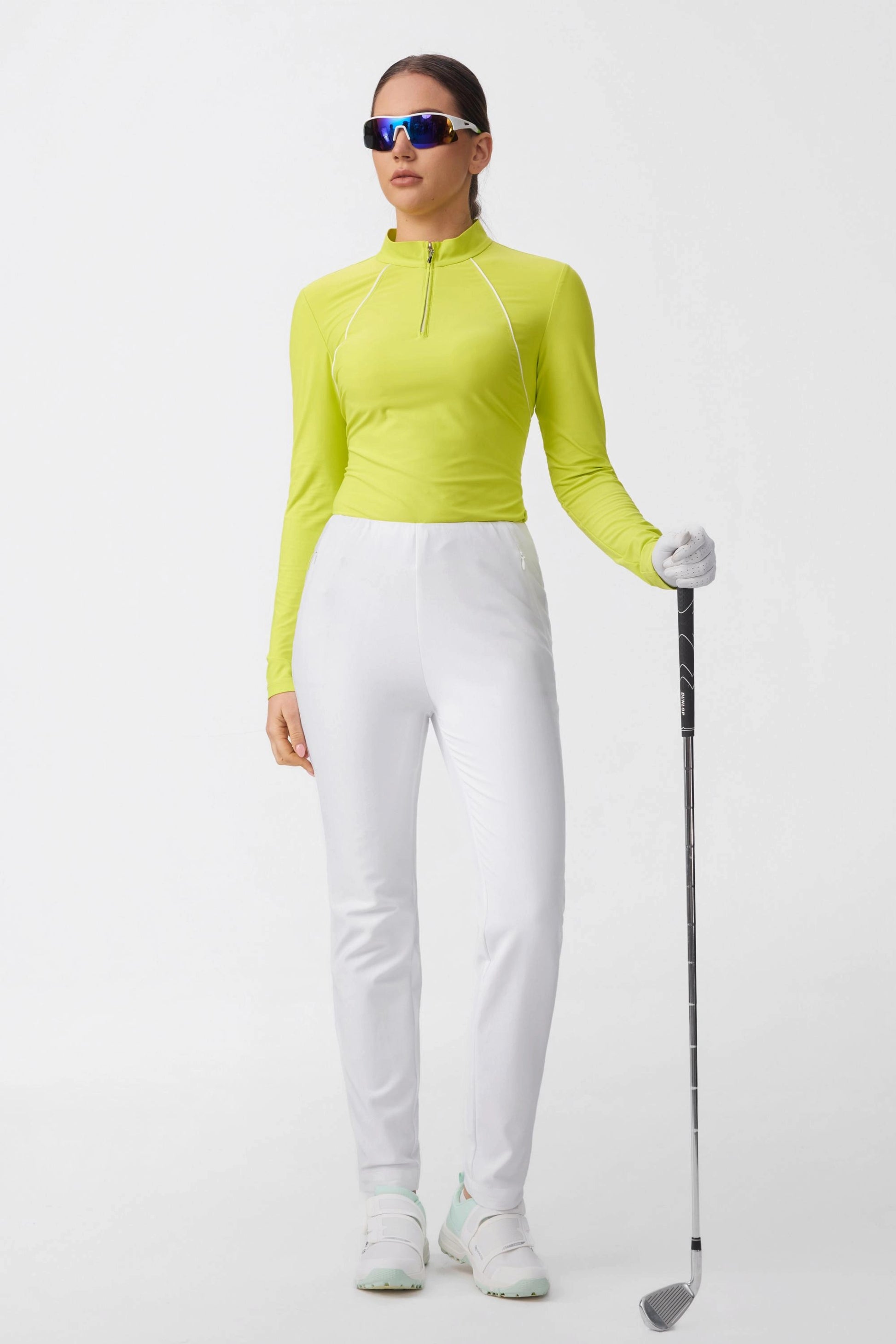 Woman wearing citron UPF 50+ quarter-zip performance golf top with white golf pants holding a golf club