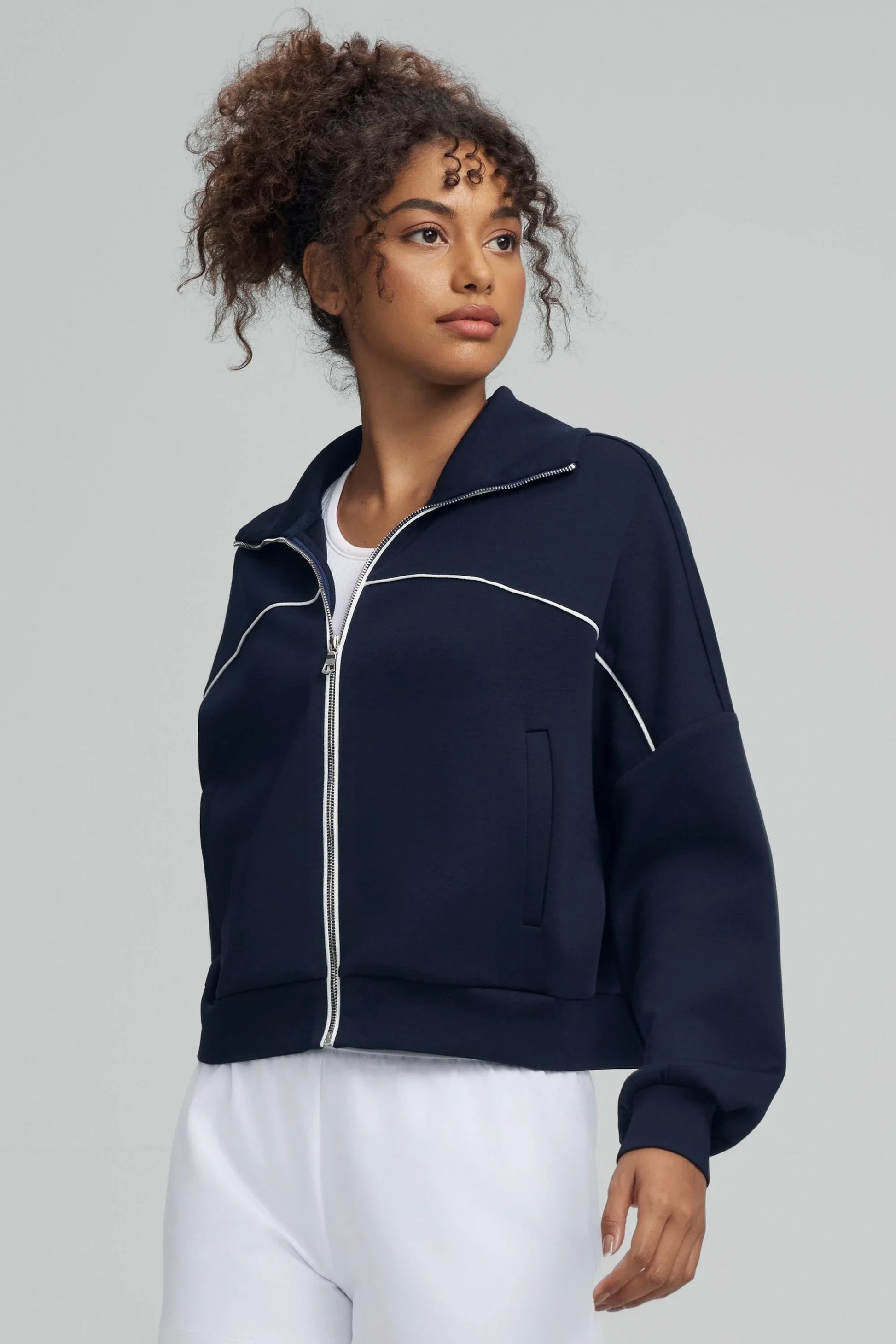 Side view of a women’s cropped golf jacket in midnight navy with contrast piping and front pockets