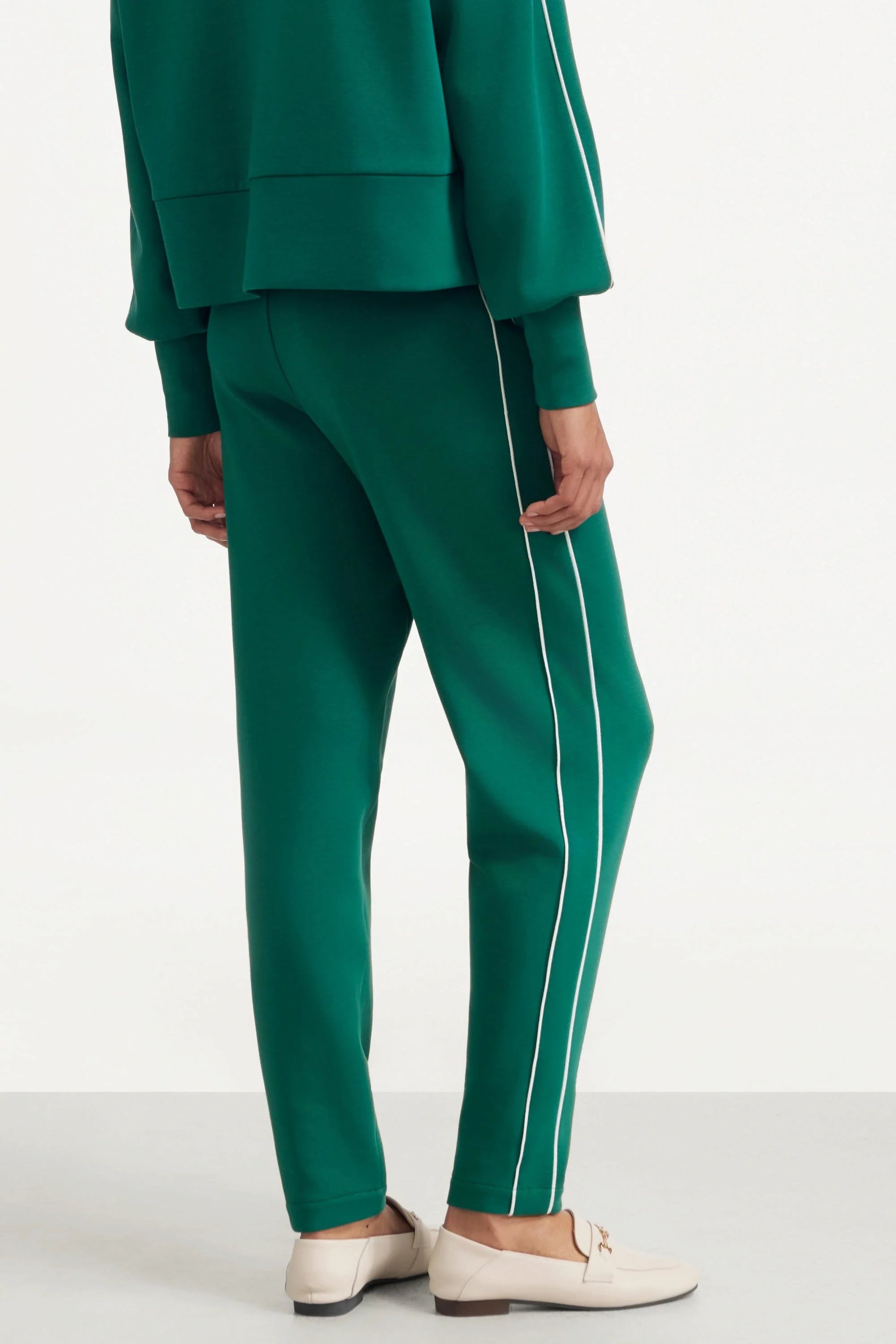 Back view of women's deep teal golf pants with contrast piping along the leg