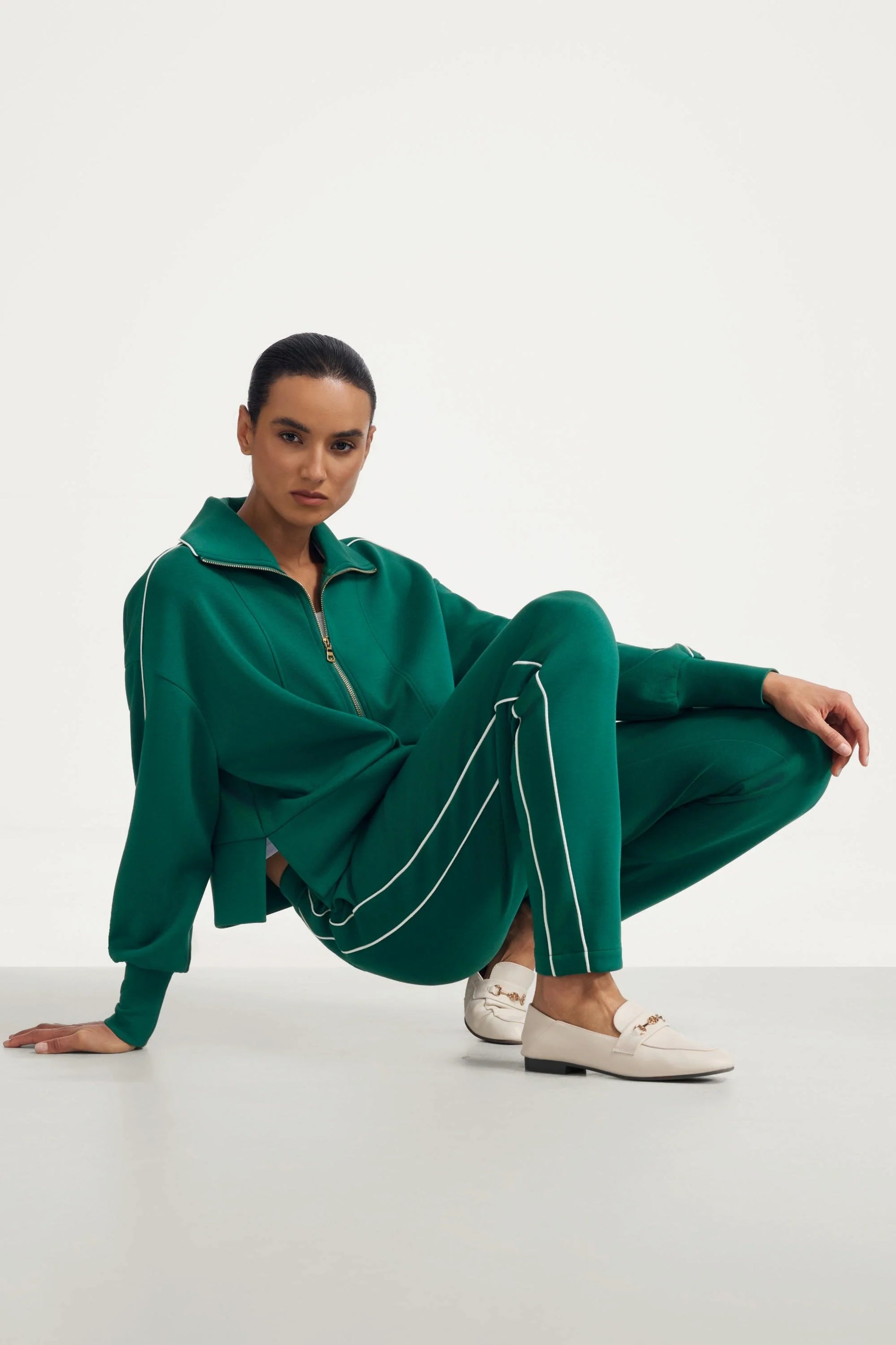 Woman wearing deep teal slim fit golf pants in a styled seated look with half zip top