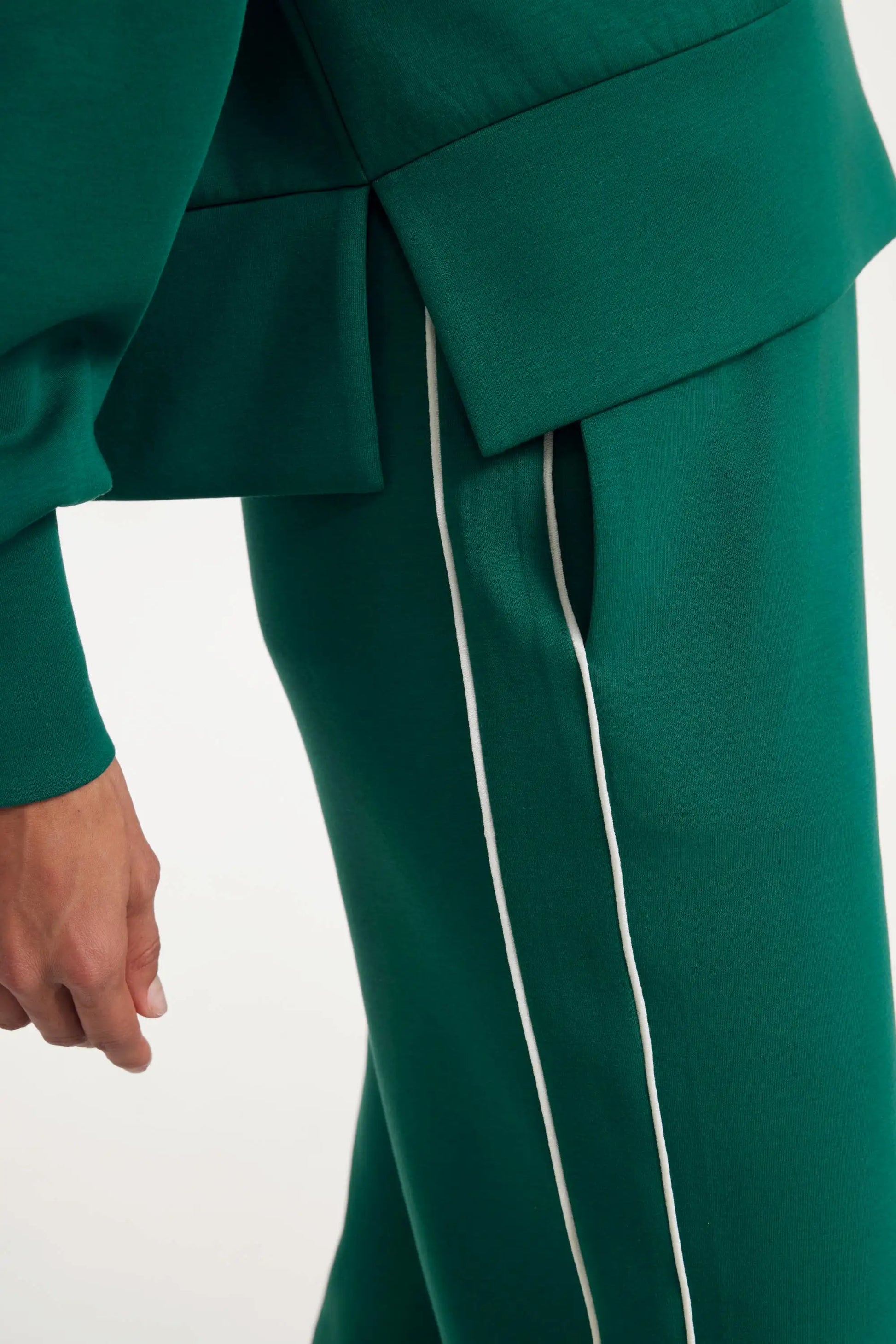 Close-up of the waist and side seam detail on deep teal track pants with contrast piping