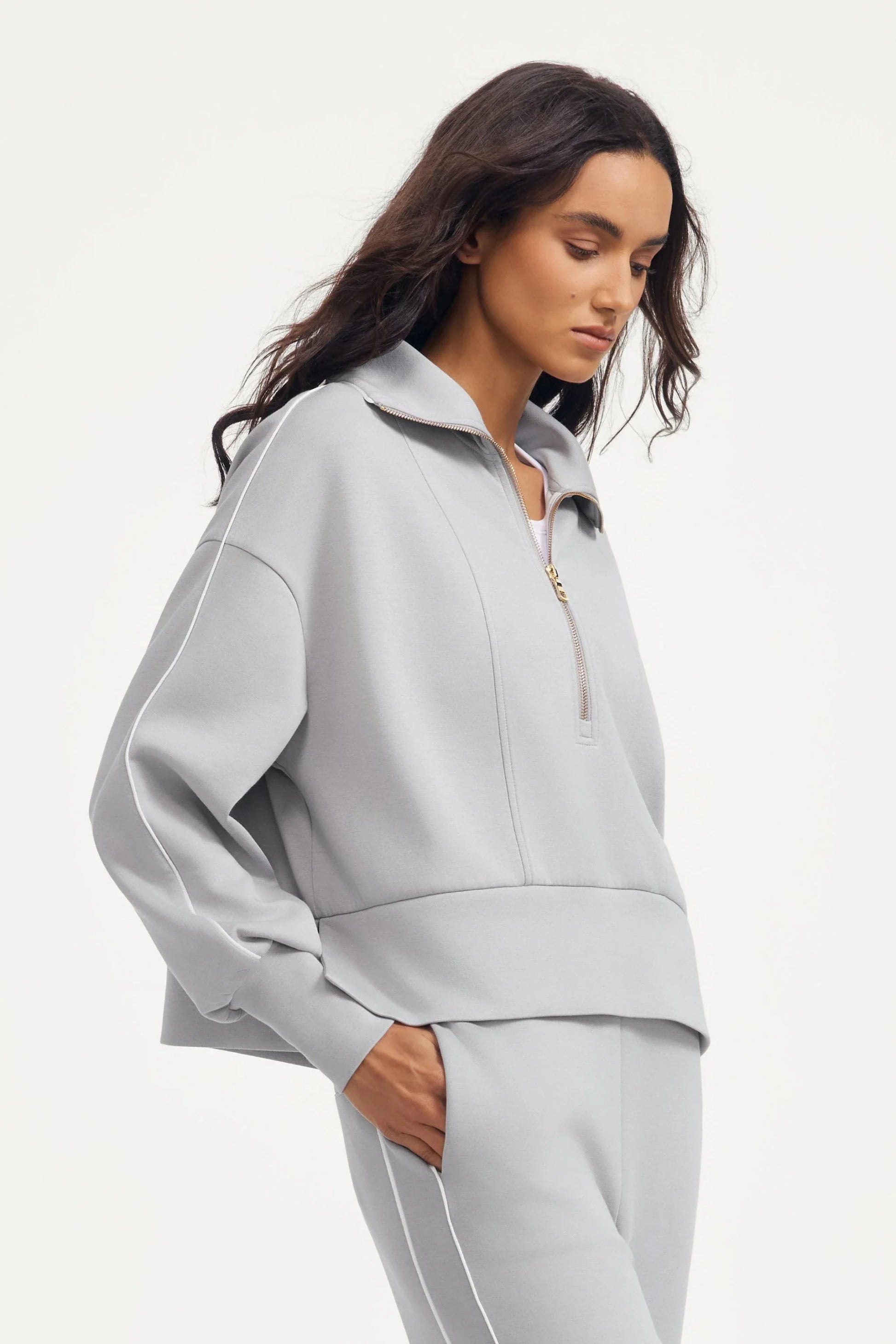 Side view of a women’s half-zip golf pullover in Soft Cloud Grey styled with matching slim fit pants