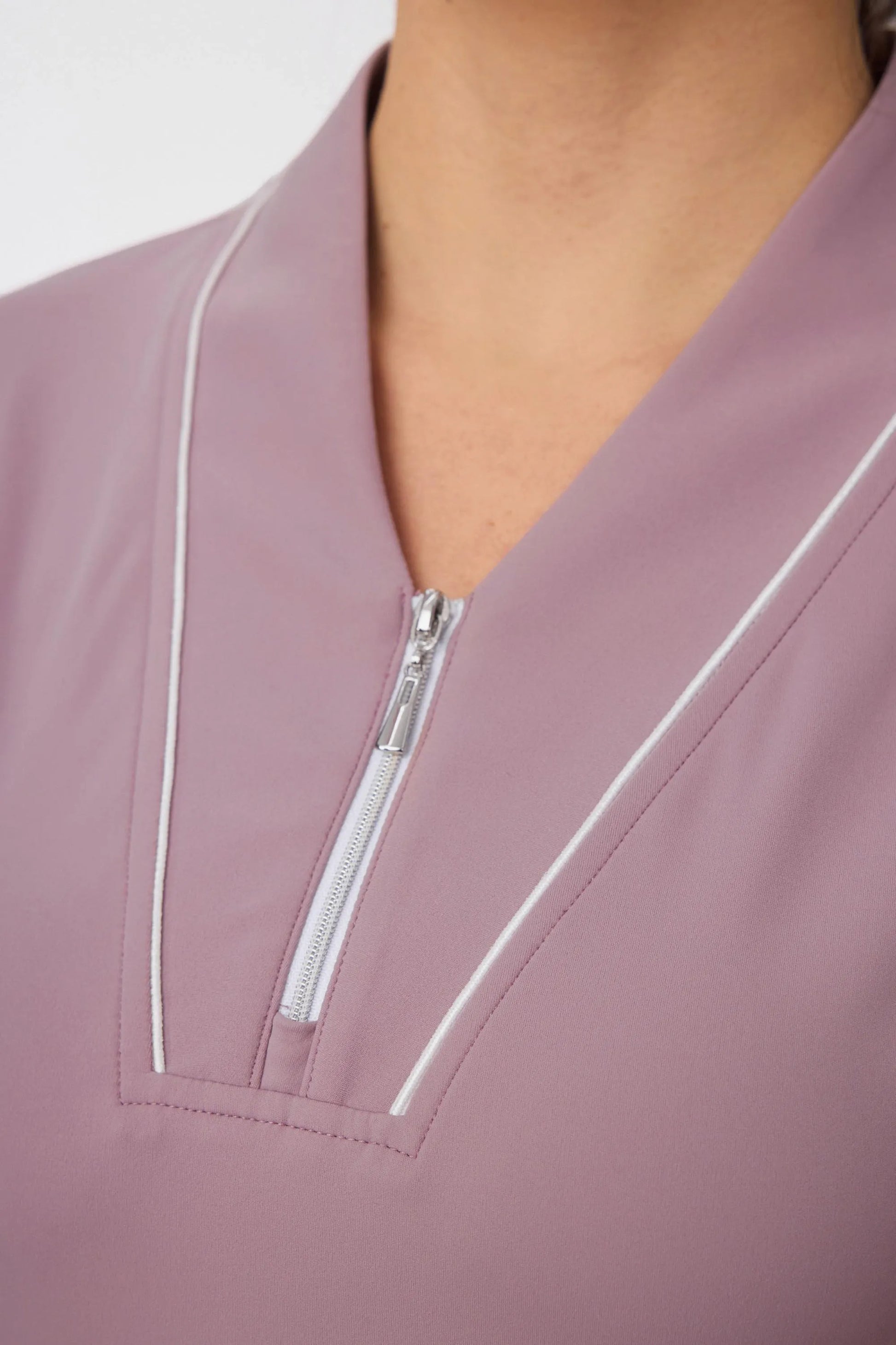 Close-up of the zip-front neckline and contrast piping on a soft mauve golf dress