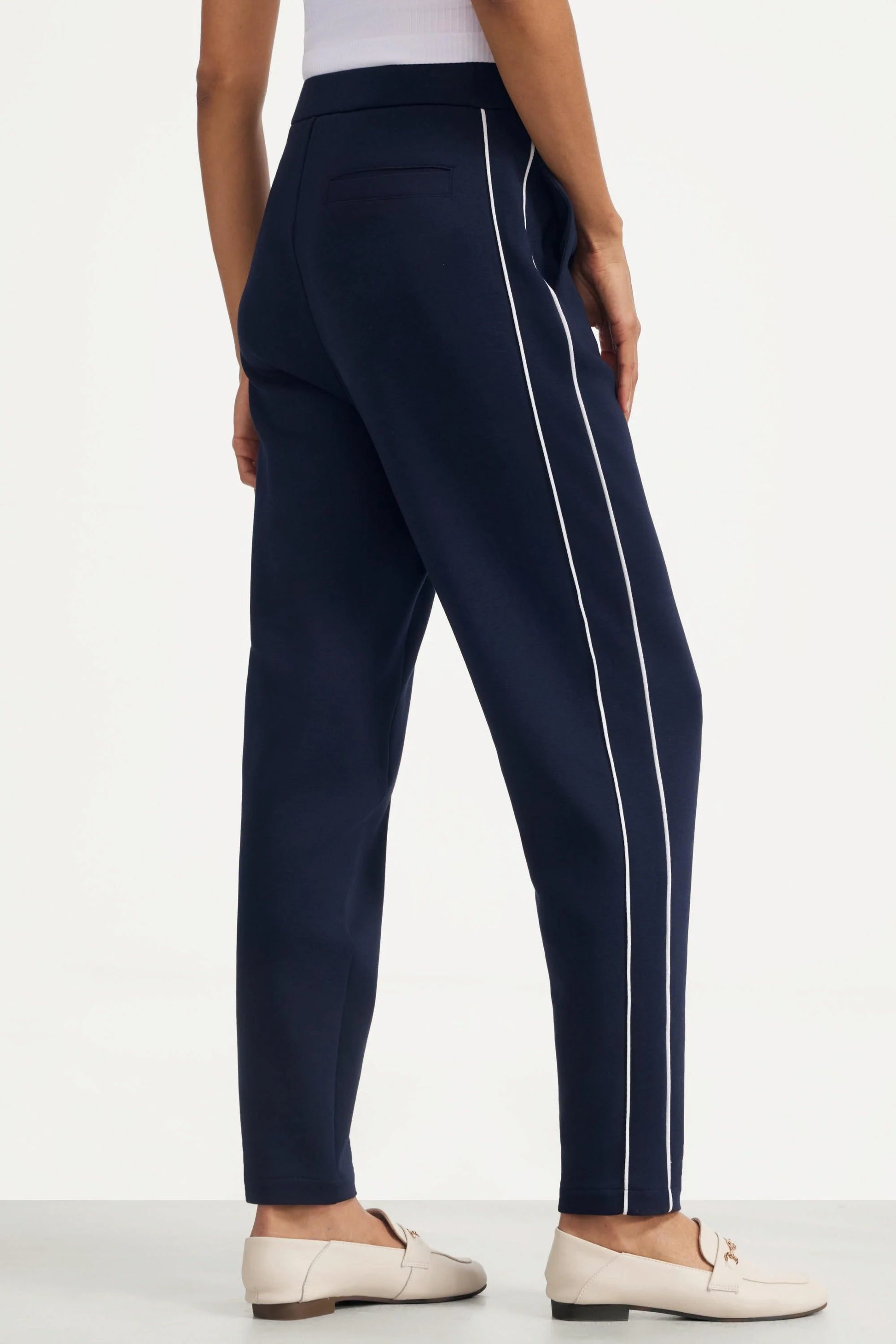 Back angled view of women's Midnight Navy golf pants with contrast piping