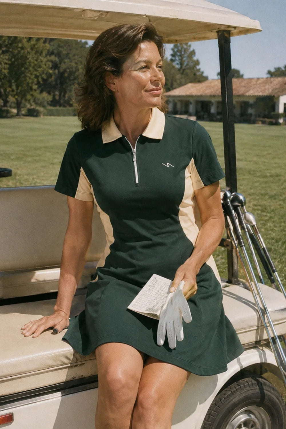 Woman wearing a No.18 Club dark green and cream colorblock golf dress seated on a golf cart holding a scorecard and glove