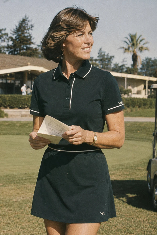 Woman wearing a No.18 Club dark green polo golf outfit holding a scorecard on the course near the clubhouse