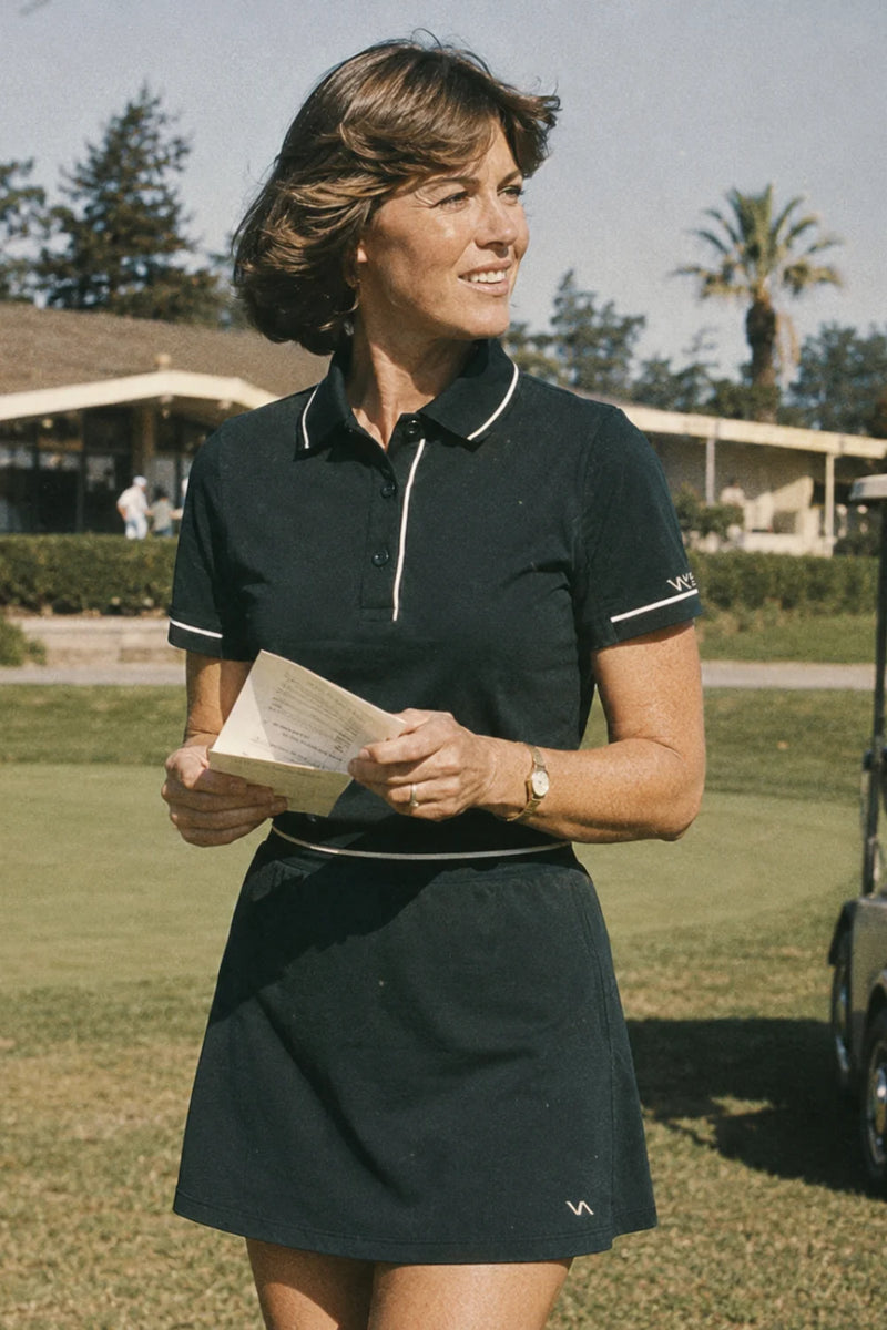 Woman wearing a No.18 Club dark green polo golf outfit holding a scorecard on the course near the clubhouse