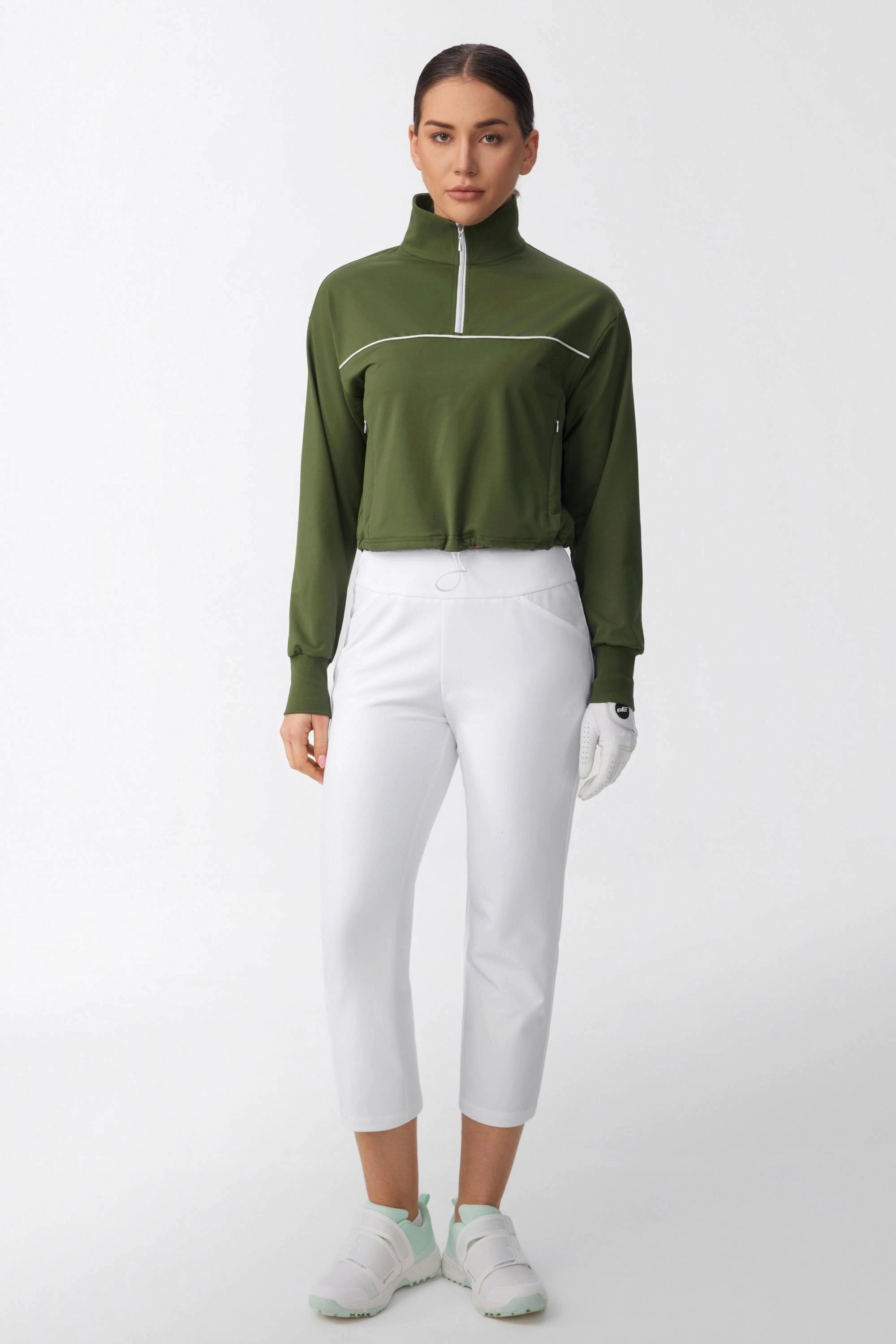 Full body view of women's olive green half-zip golf top styled with white cropped golf pants
