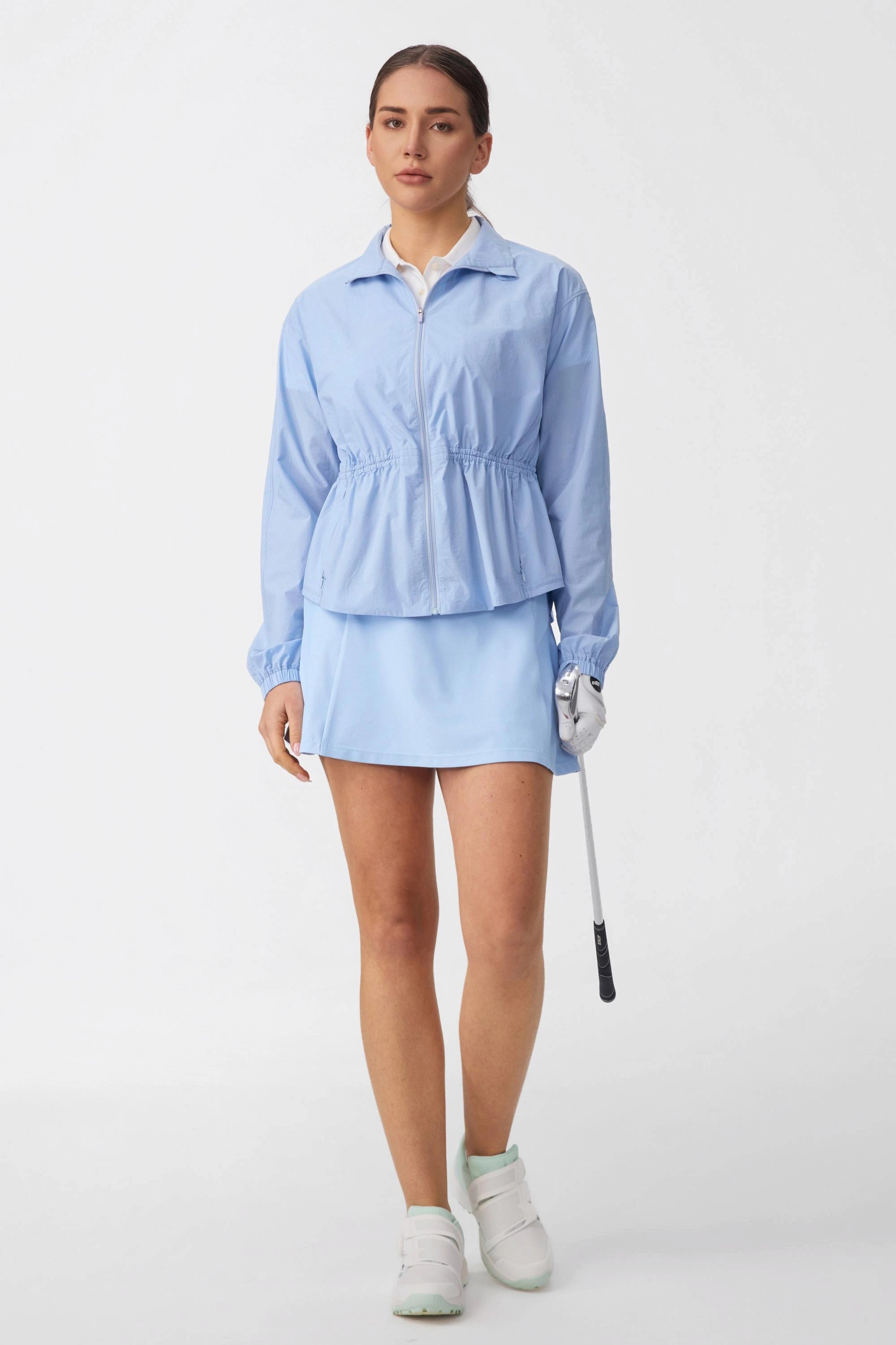 Model wearing a women’s performance golf skort in skyline blue paired with a light blue golf jacket
