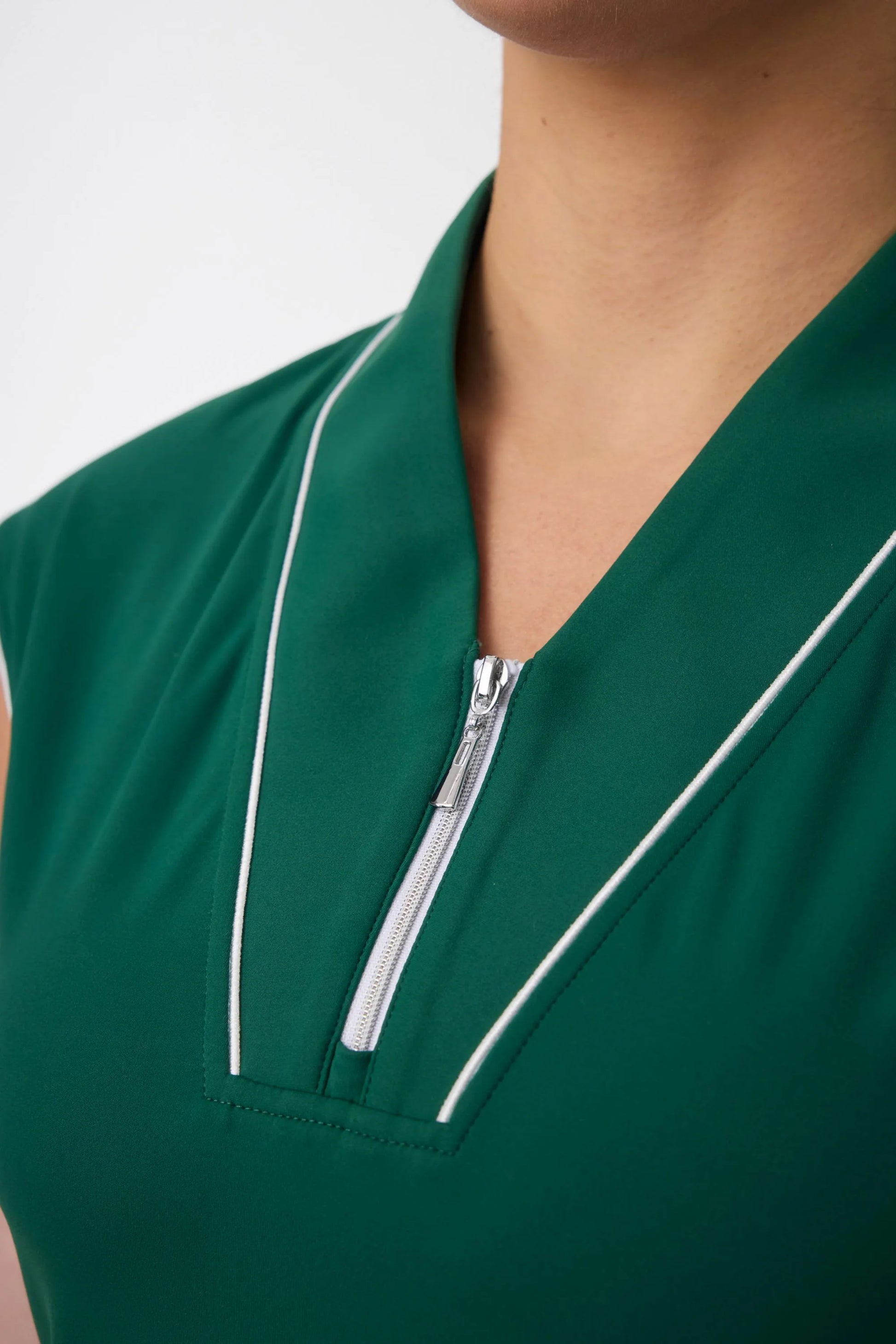 Close-up of the zip-front neckline and contrast piping on a pine green golf dress