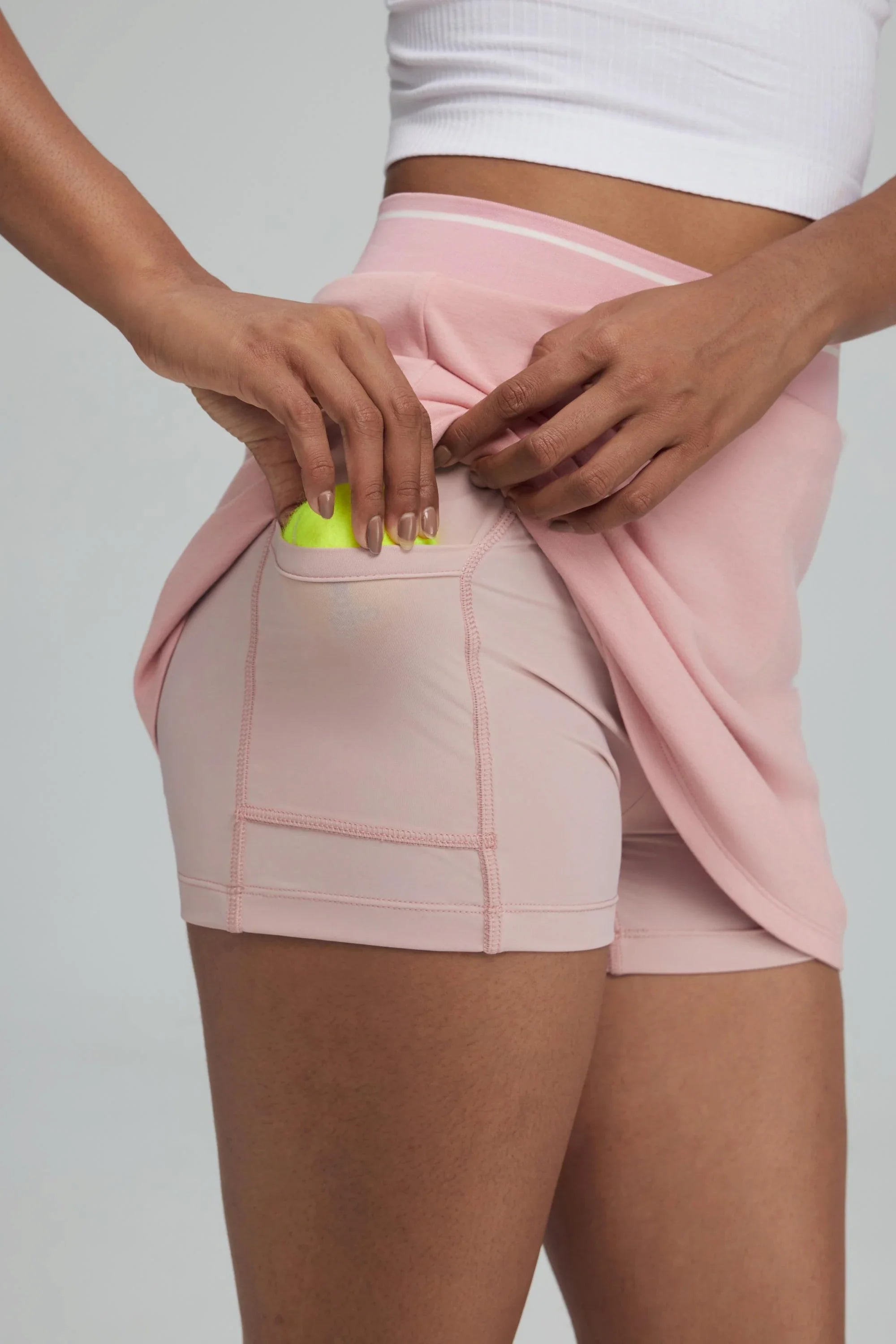 Detail of built-in shorts pocket inside a powder pink golf skort holding a golf ball