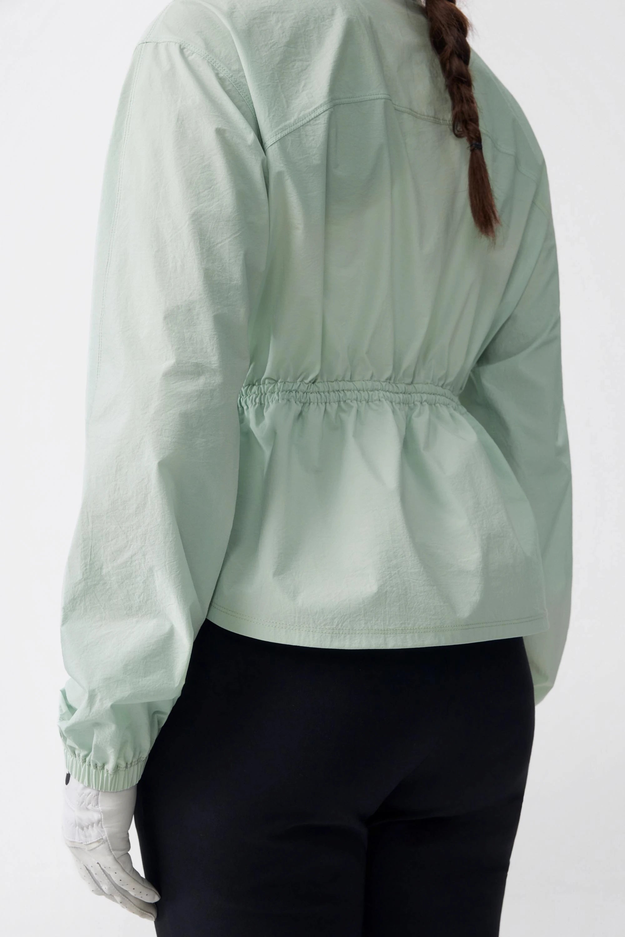 Back detail of a sage mist lightweight golf jacket highlighting the gathered waist and seam construction
