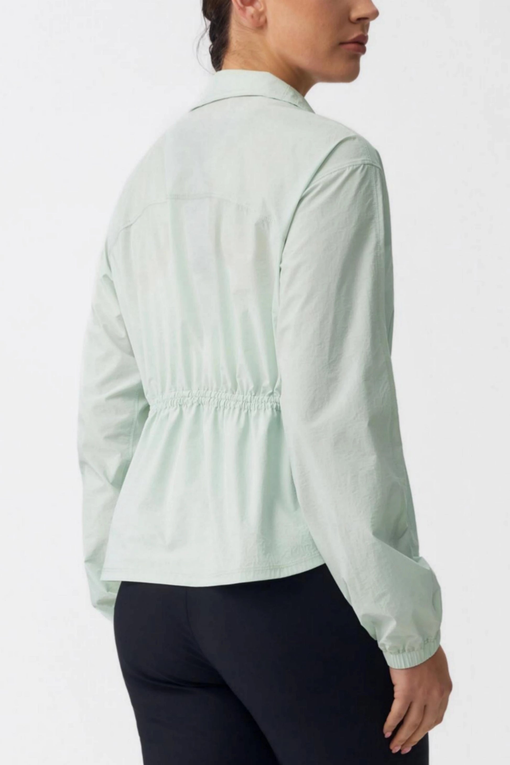 Back view of a sage mist lightweight golf jacket showing the gathered cinched waist design