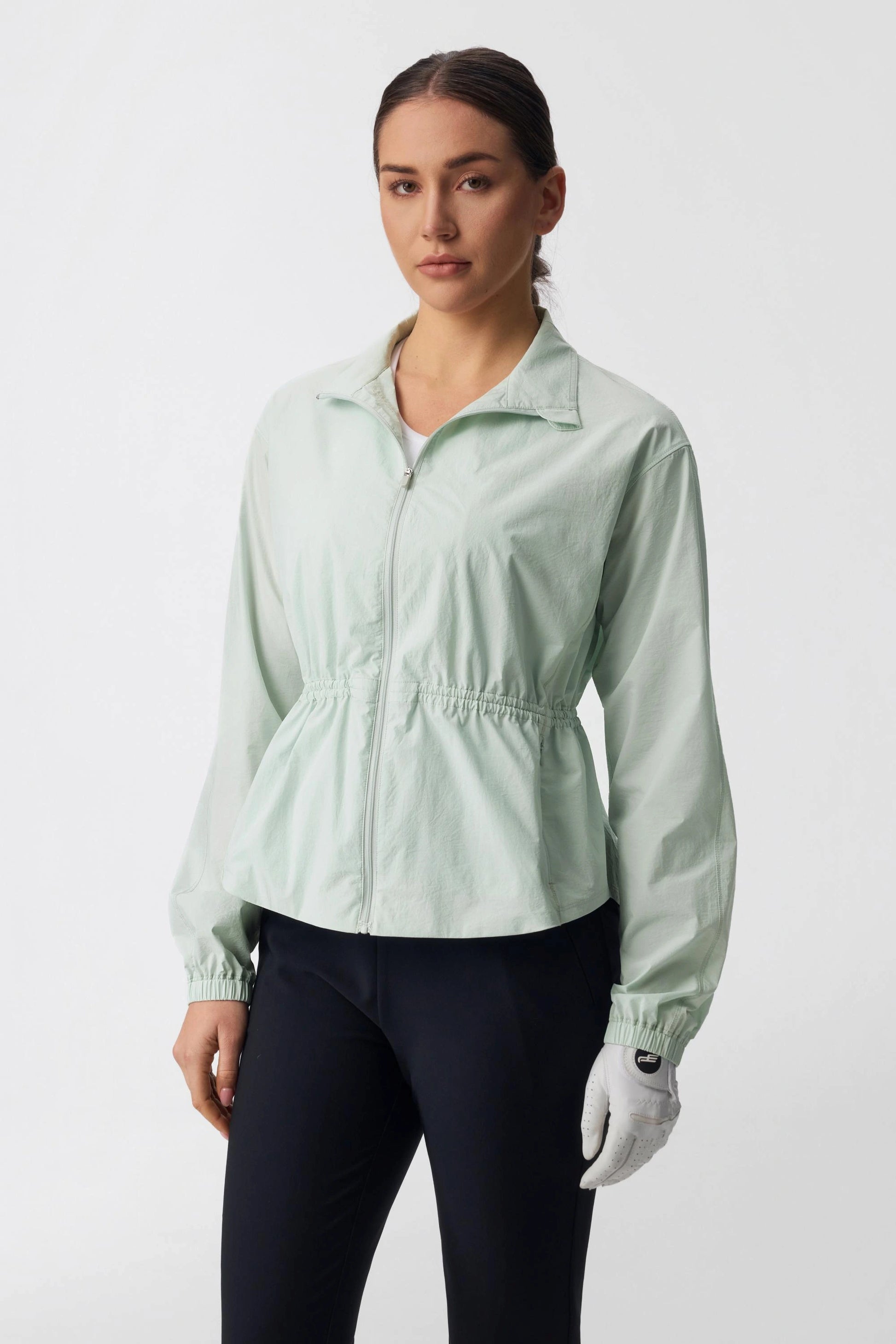 Model wearing a sage mist lightweight golf jacket with a flattering cinched waist and zip front