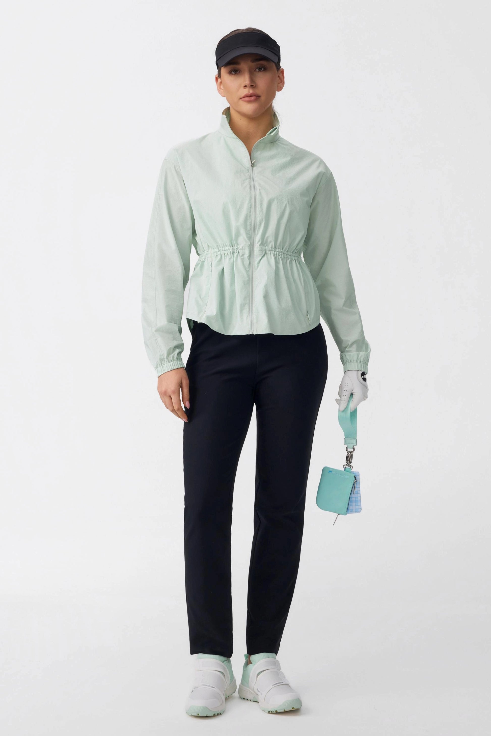 Golfer wearing a sage mist lightweight golf jacket with navy golf pants, visor, and golf glove