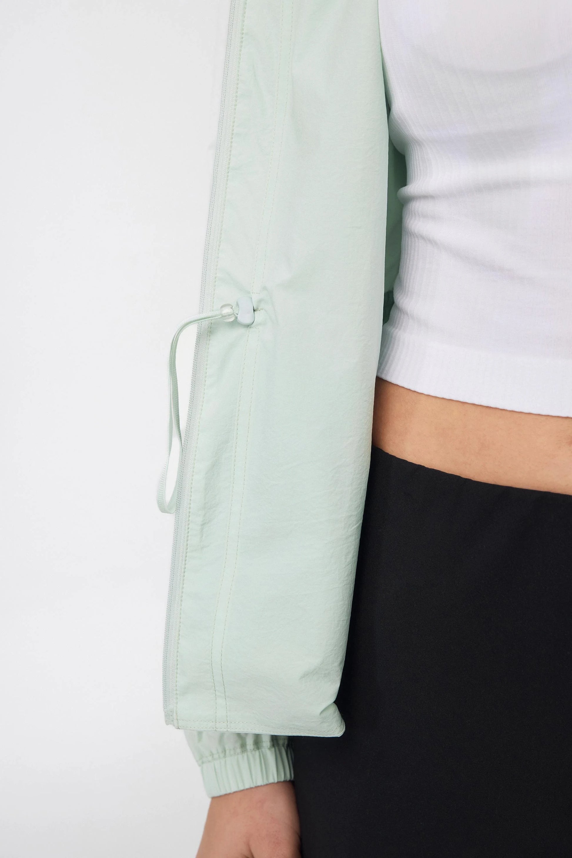 Close-up of the adjustable drawcord at the hem of a sage mist lightweight golf jacket