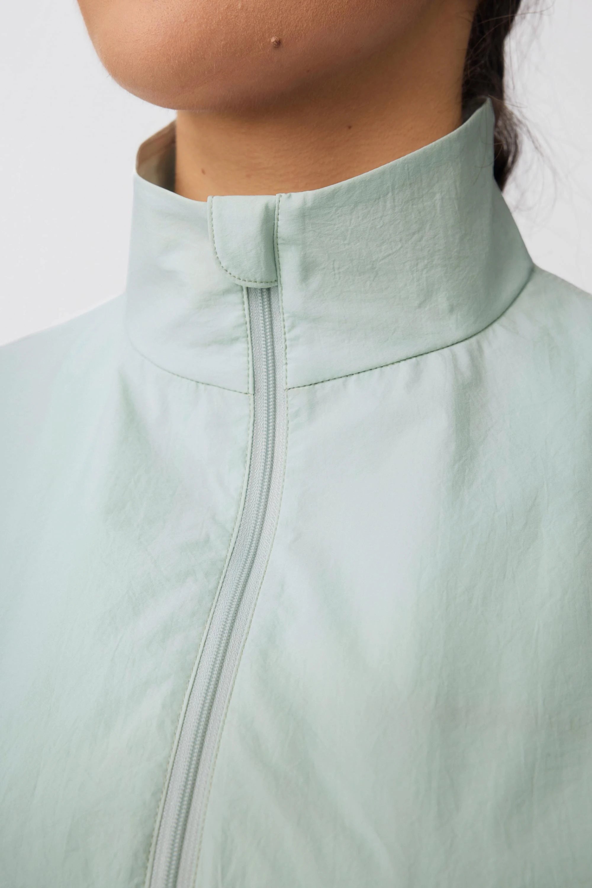 Close-up of the stand collar and front zipper on a sage mist lightweight golf jacket