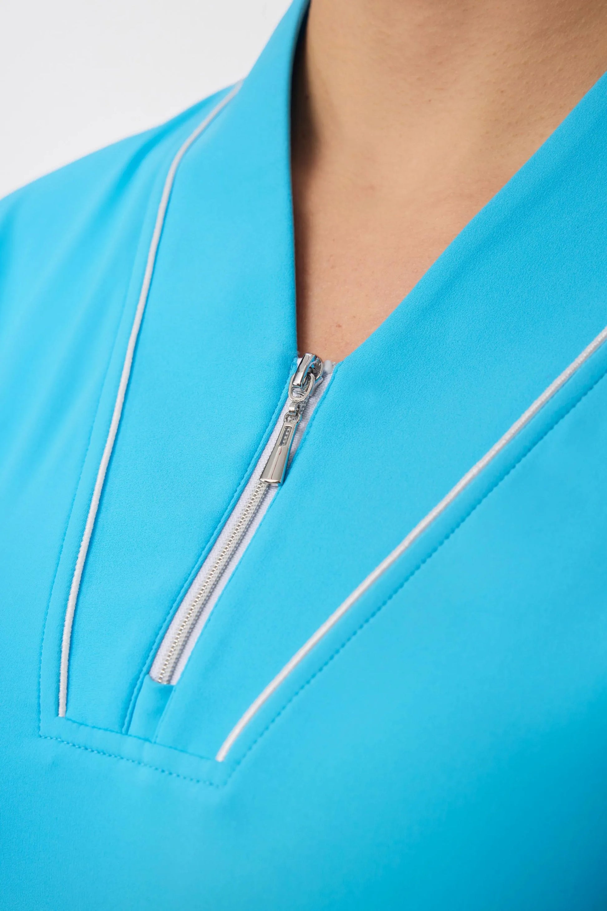Close-up of the zip-front neckline and contrast piping on a sky blue golf dress