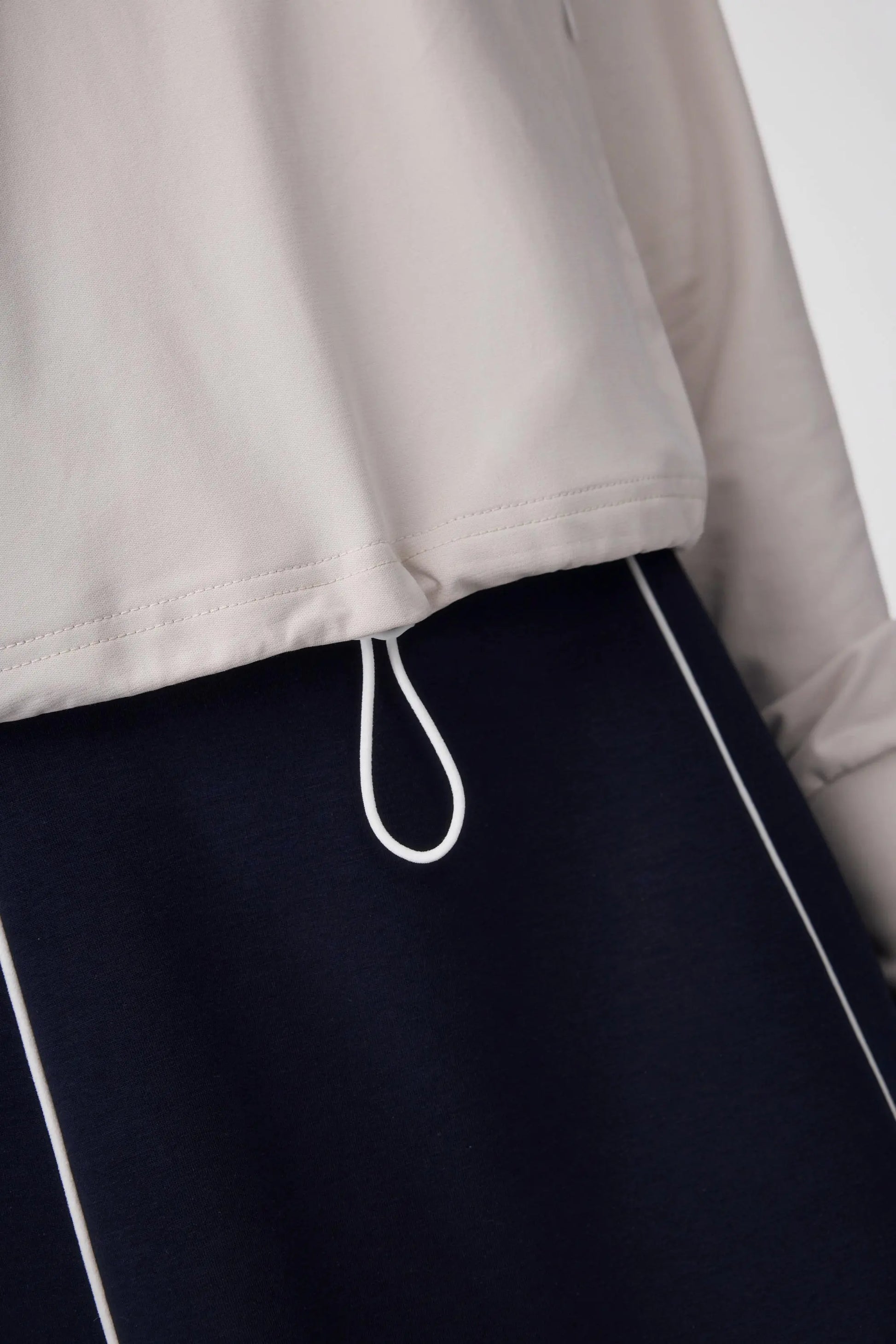 Close-up of the hem drawcord detail on a soft taupe half-zip golf top