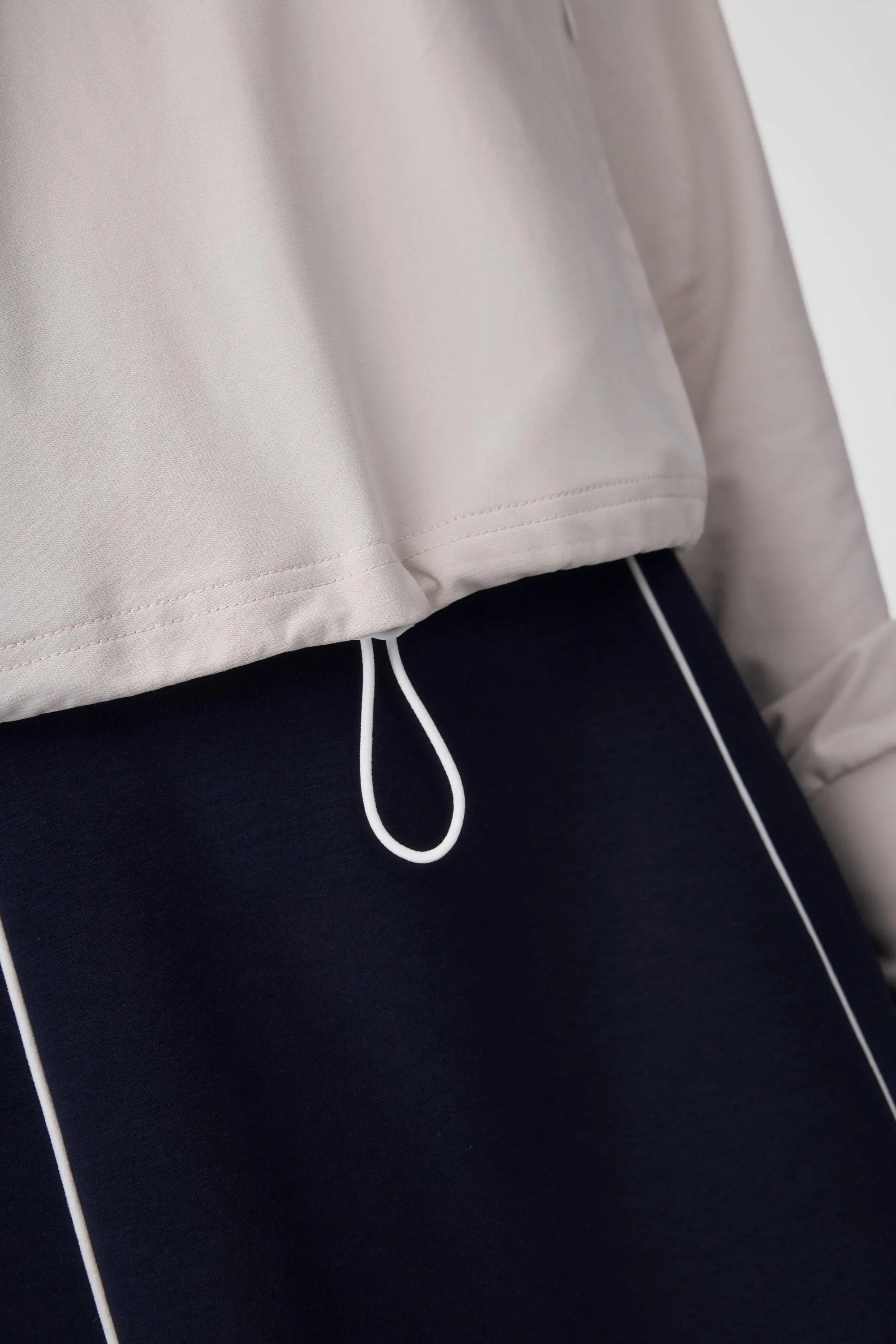 Close-up of the hem drawcord detail on a soft taupe half-zip golf top