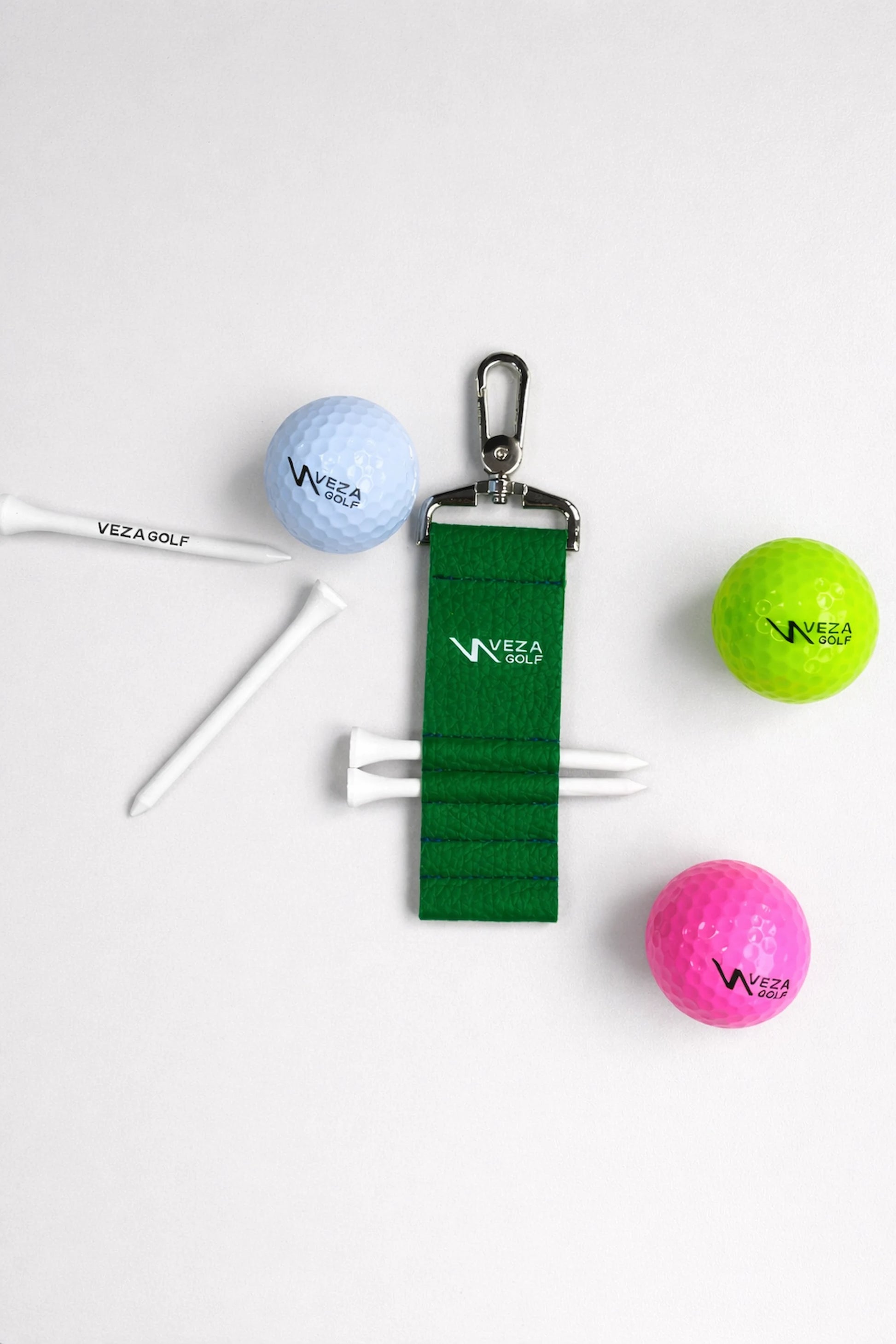 VEZA green golf tee holder with metal clip holding tees, displayed with colorful VEZA golf balls and golf tees