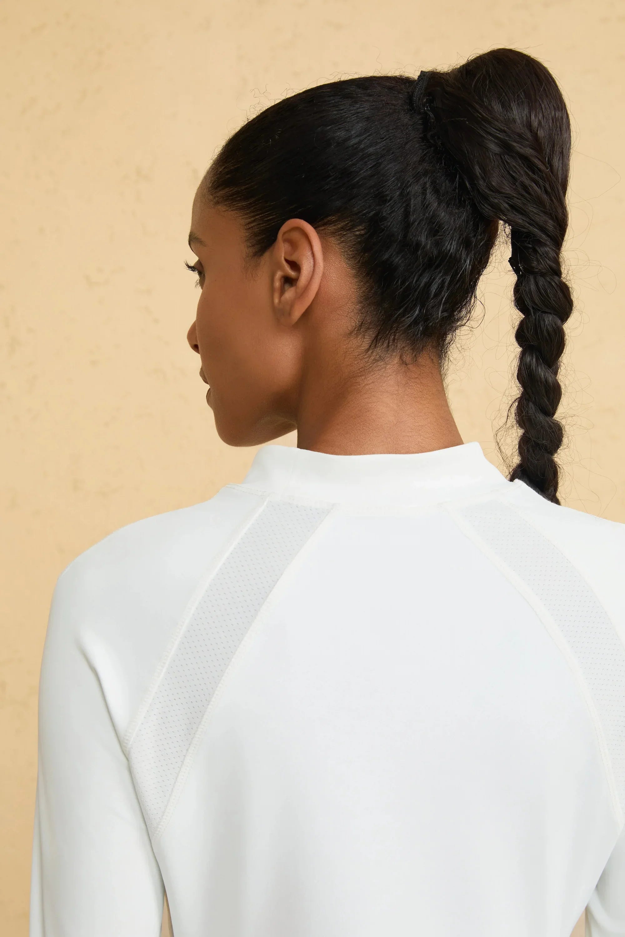 Close-up of VEZA cloud white mock-neck performance top showing breathable, seamless shoulder fabric detail