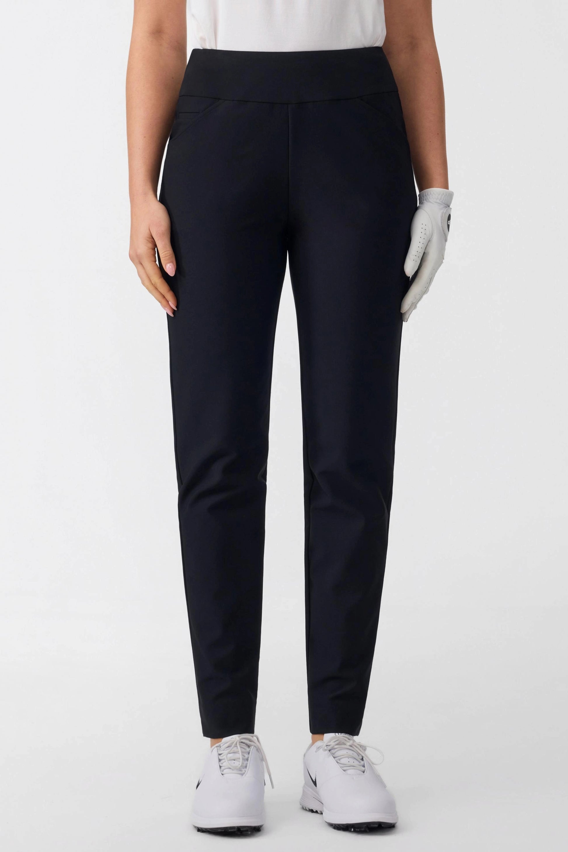 Front view of women’s onyx black tapered golf pants paired with a white golf polo
