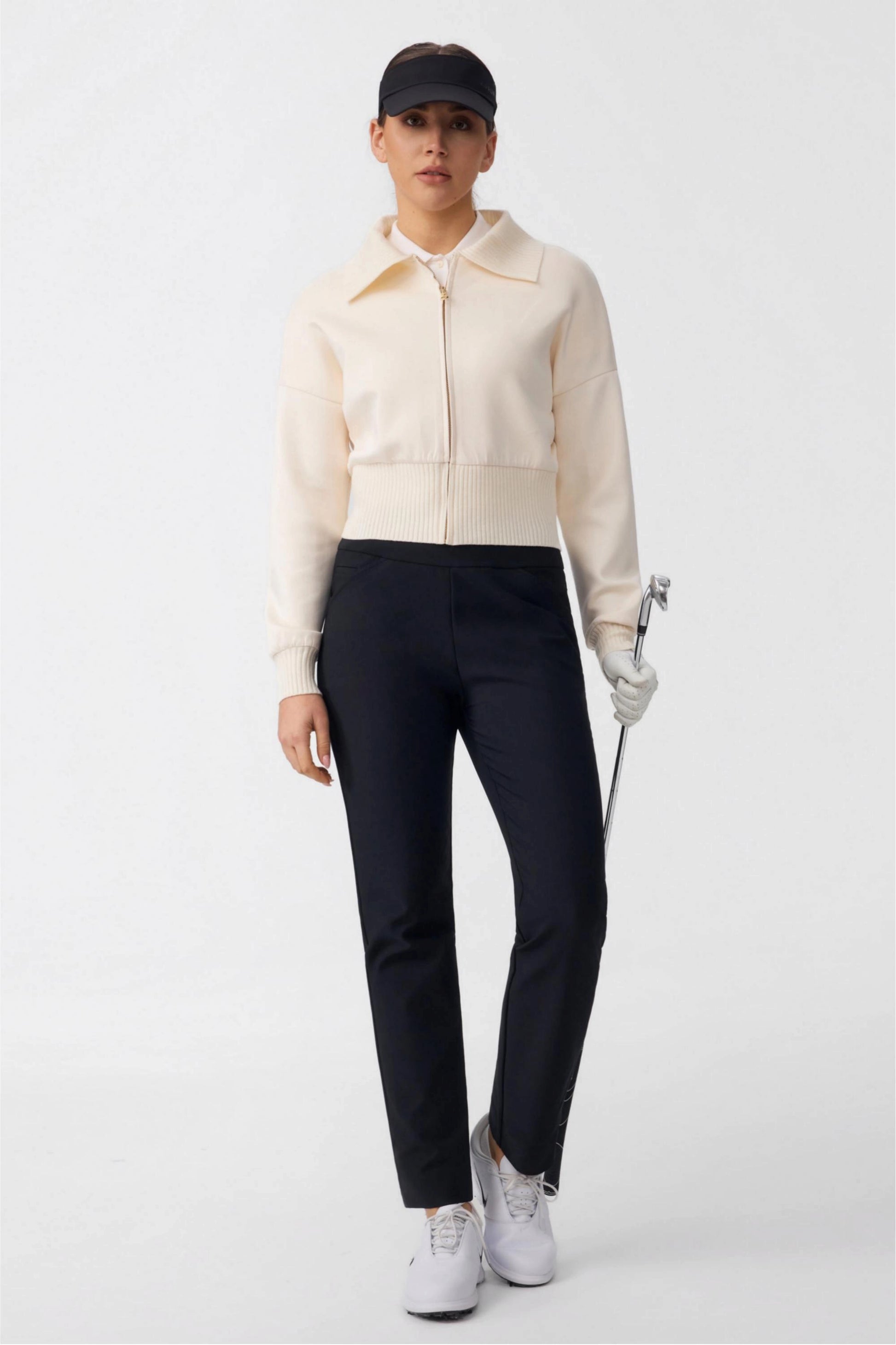 Full outfit view of women’s onyx black tapered golf pants styled with a cream golf jacket