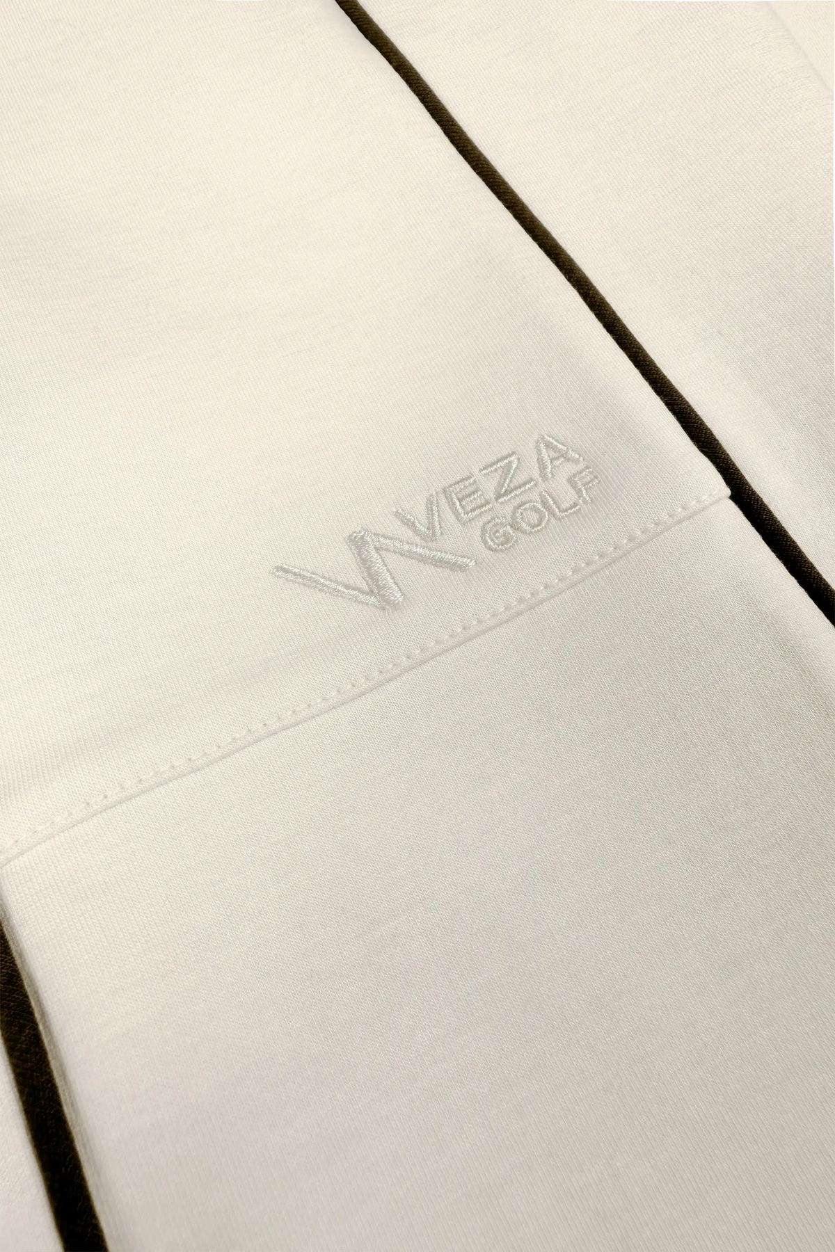 Close-up of women’s ivory barrel leg pants with embroidered VEZA GOLF logo and dark contrast piping
