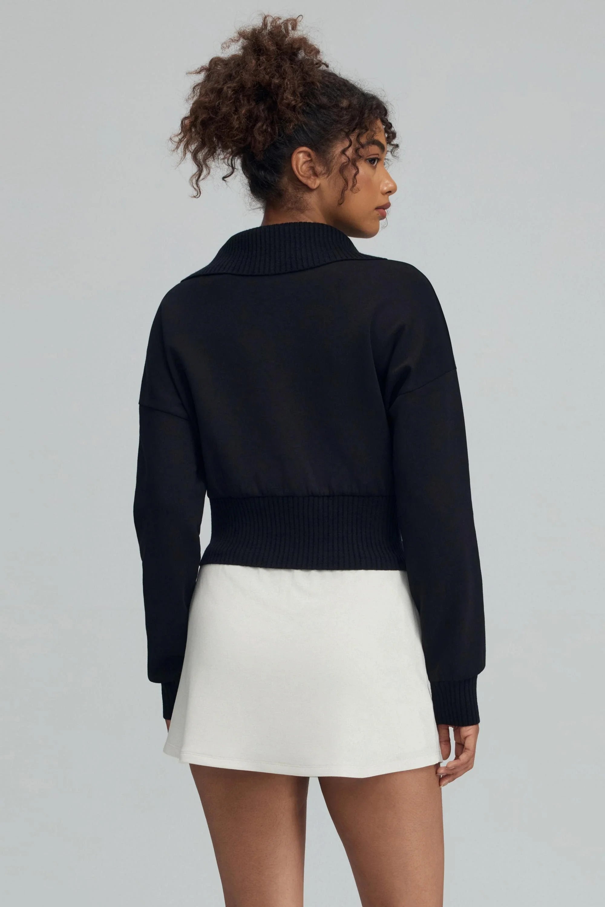Back view of women’s black cropped knit zip jacket with cropped silhouette