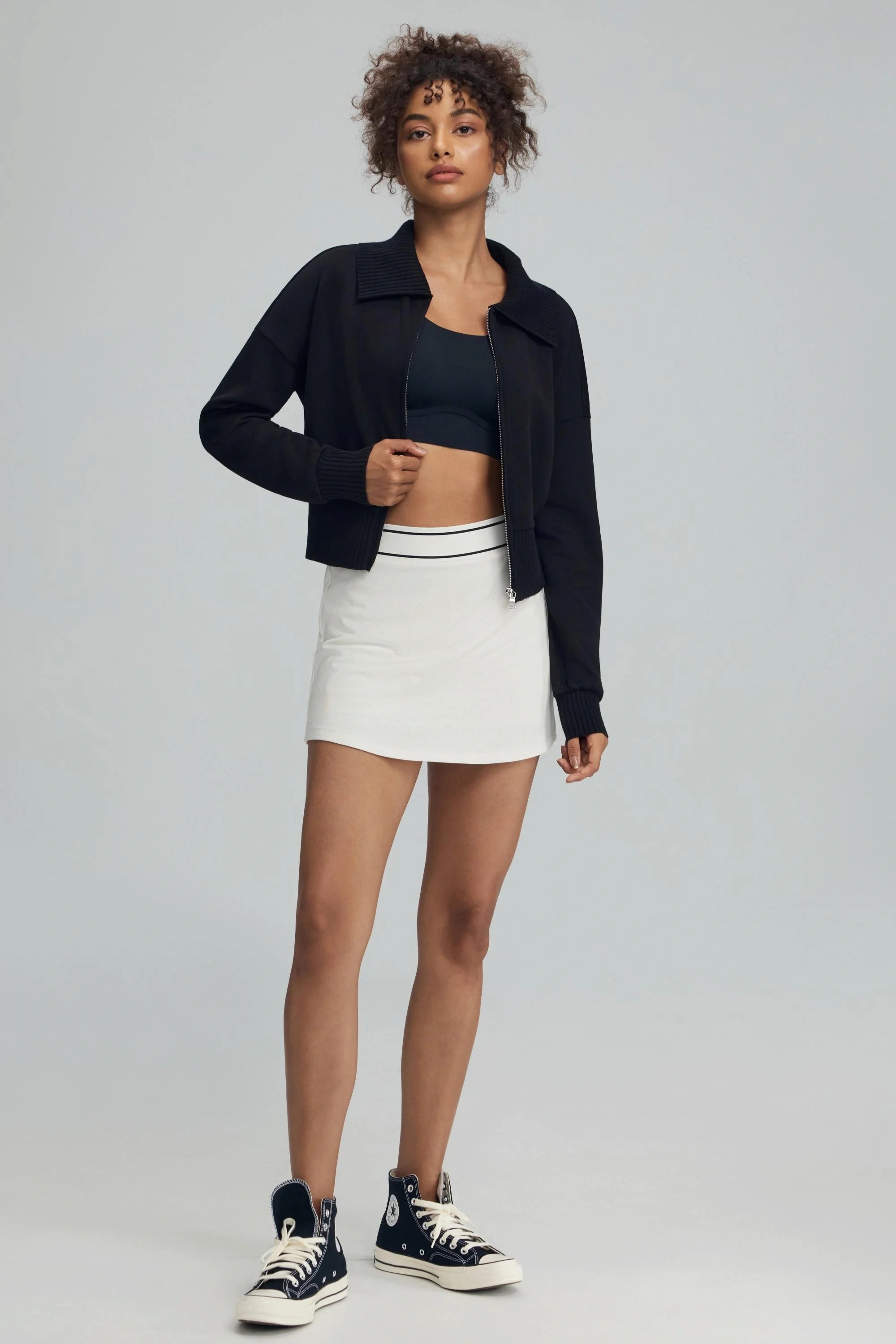 Women’s black cropped knit zip jacket paired with white golf skort