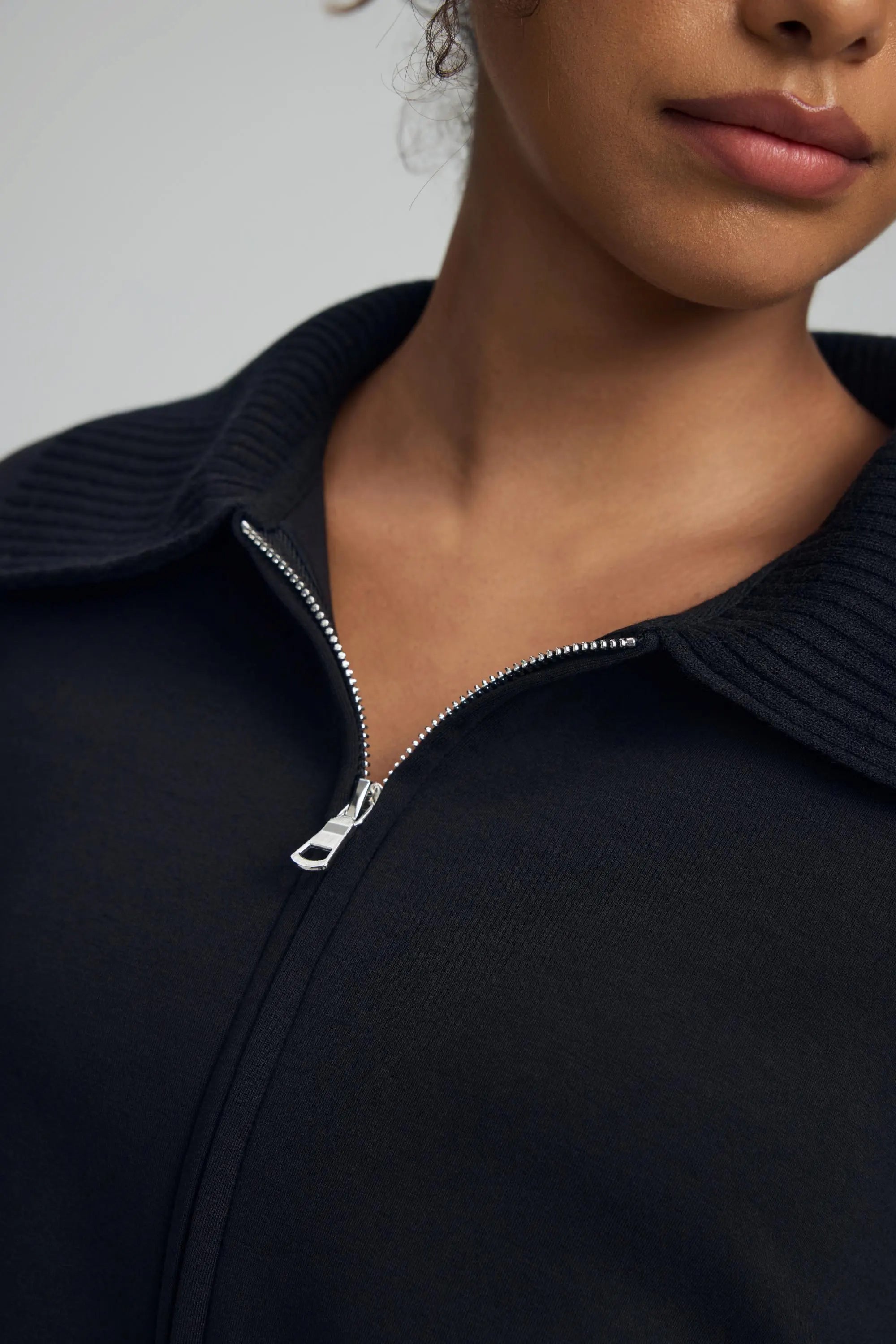 Close-up zipper detail of women’s black cropped knit zip jacket