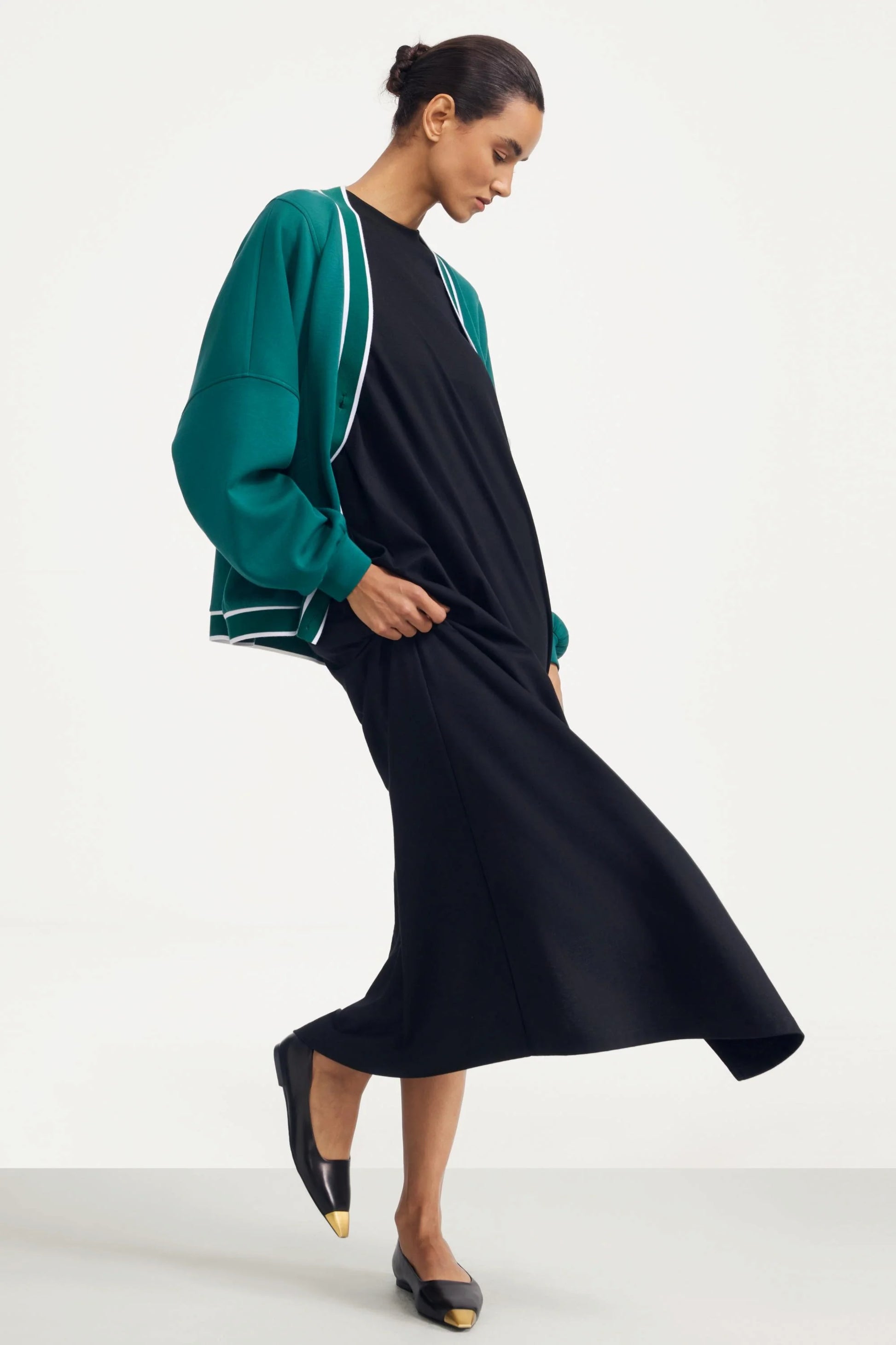 Side view of a deep teal women’s button cardigan styled with a flowing navy dress