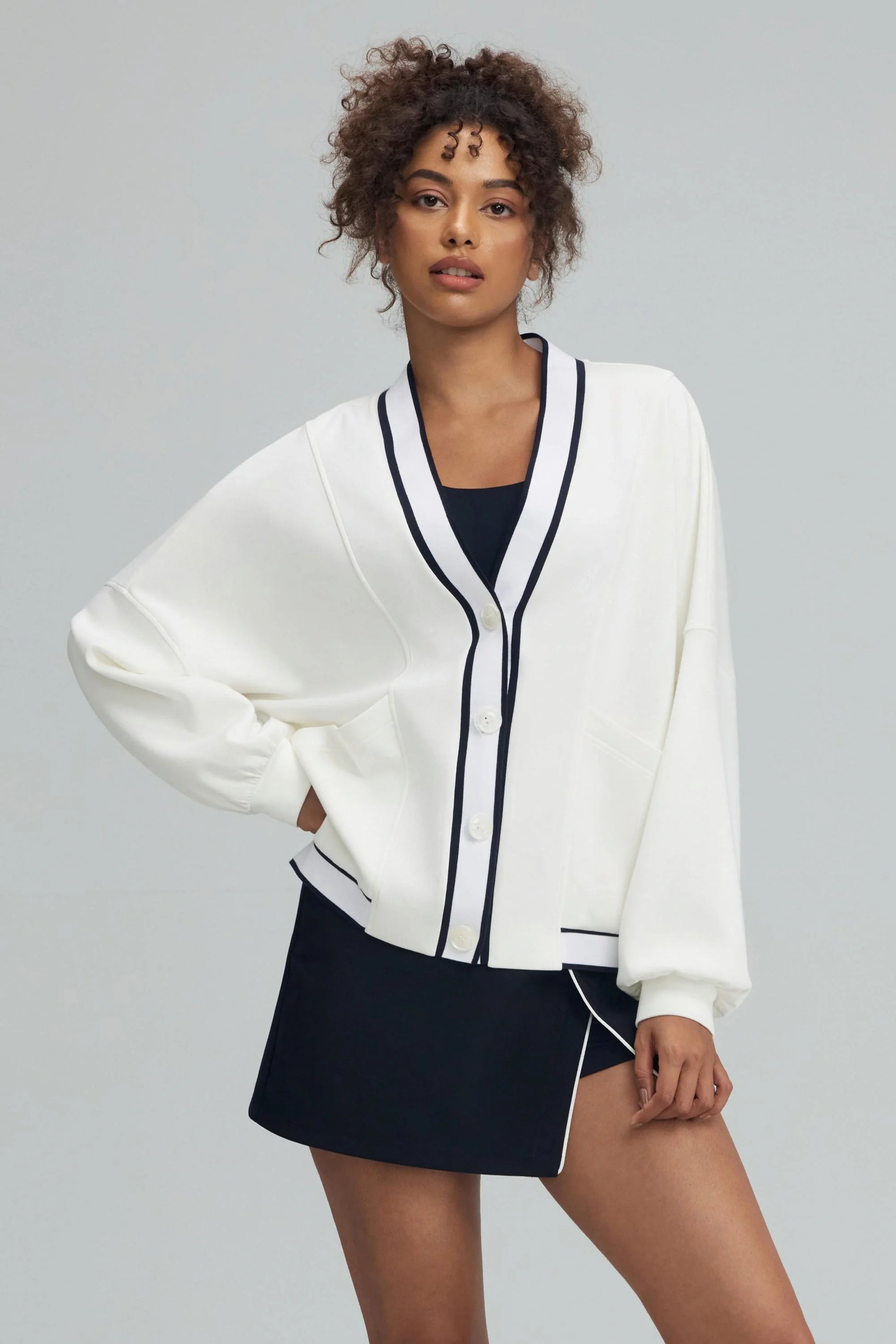 Women’s button cardigan in soft ivory with contrast trim, styled with a navy golf skirt