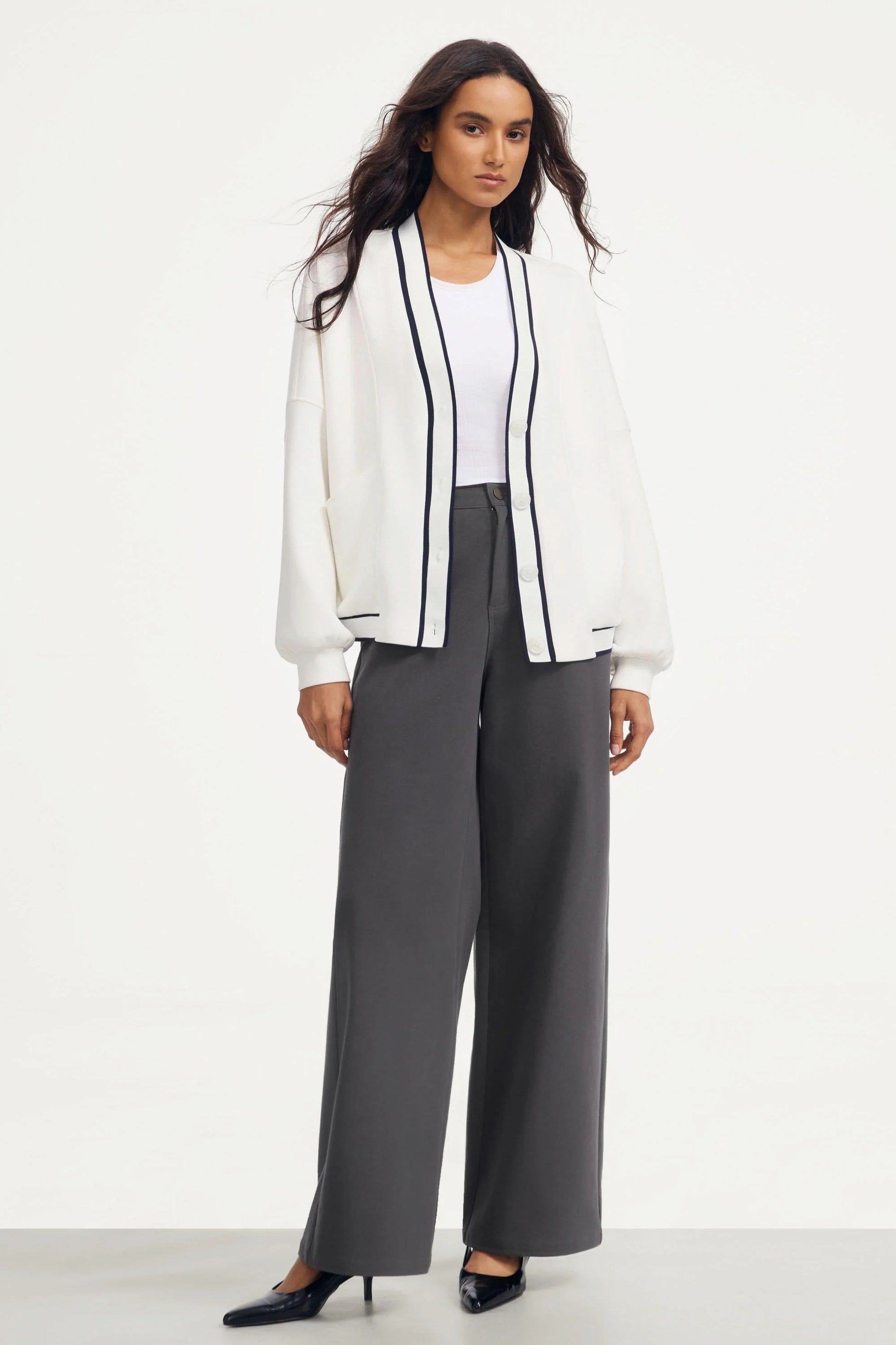 Woman wearing a soft ivory button cardigan with a white tank and charcoal wide-leg pants