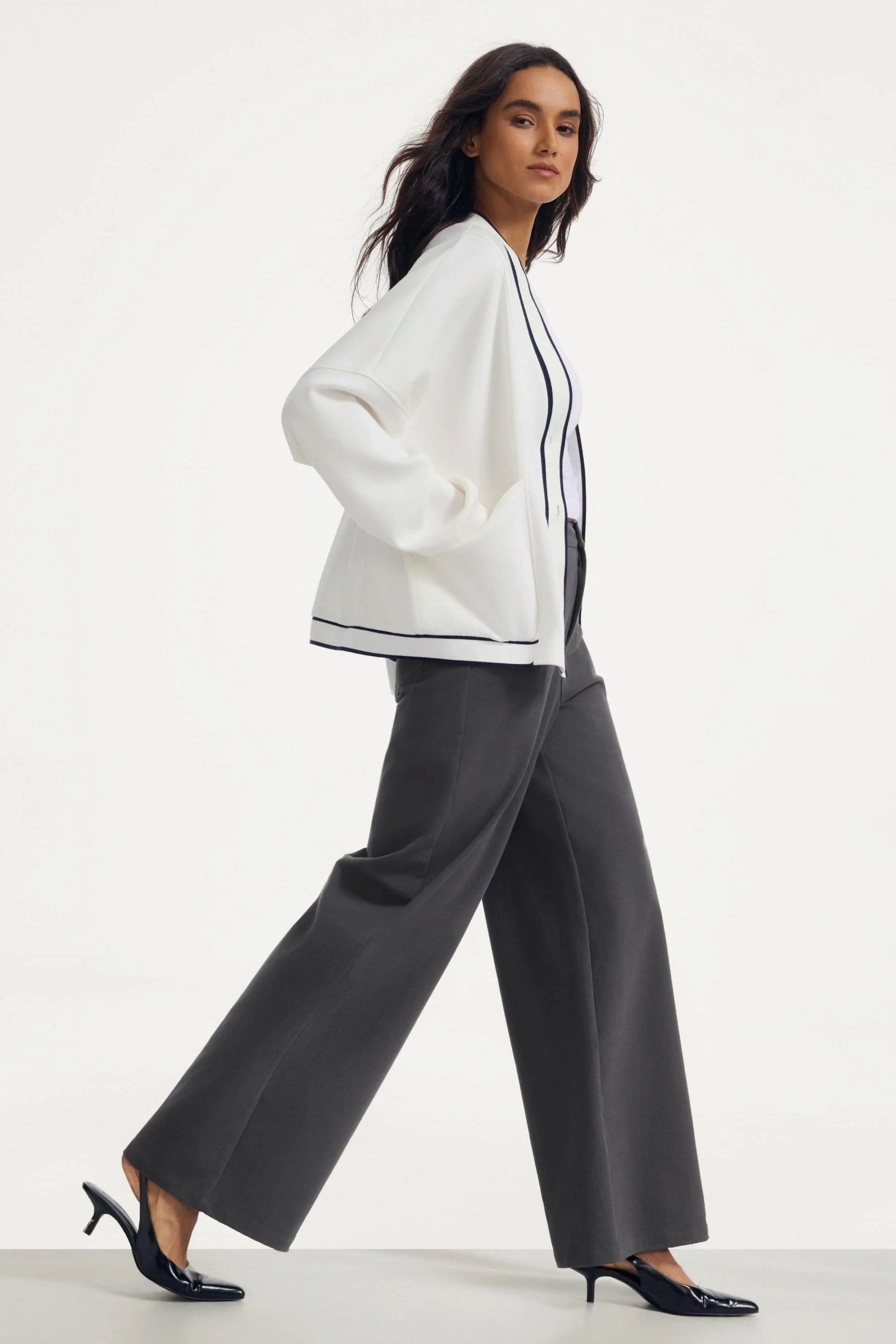 Woman walking in a soft ivory button cardigan with contrast trim and charcoal wide-leg pants