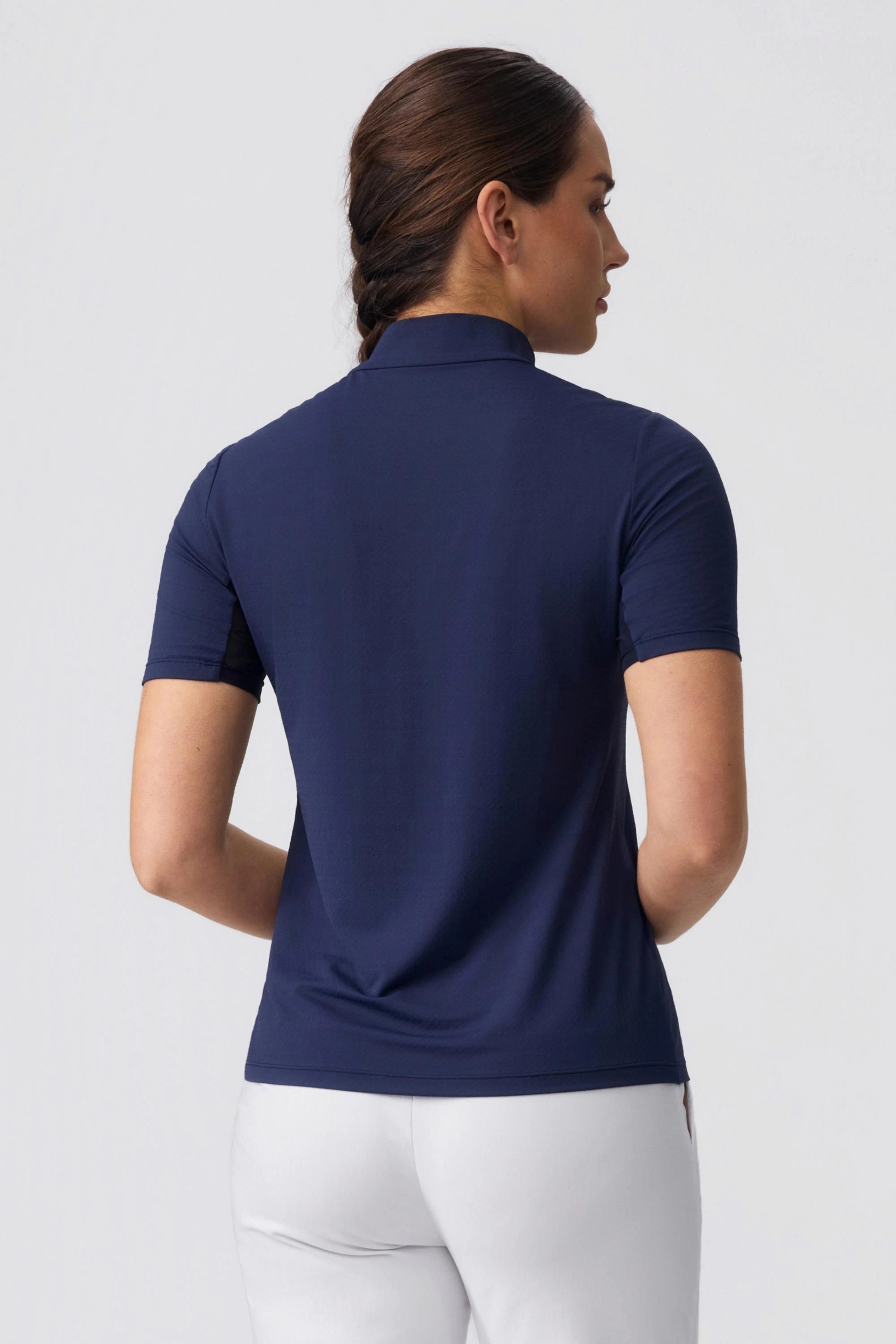 Back view of model wearing a navy contour zip neck golf top with a sleek fitted design