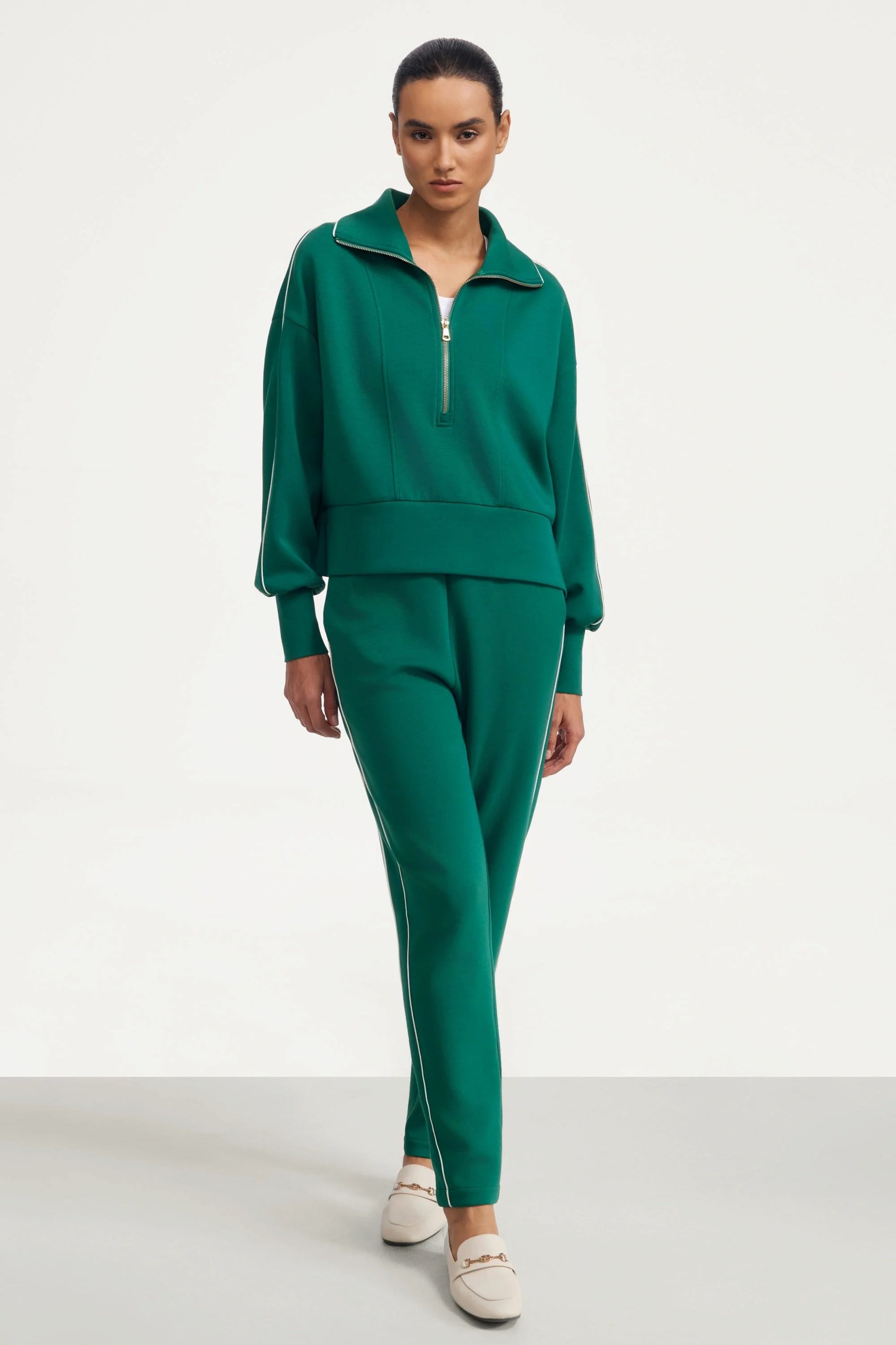 Woman wearing deep teal slim fit golf pants styled with a matching half-zip top