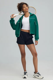 Woman wearing a green golf jacket with athletic shorts holding a tennis racket