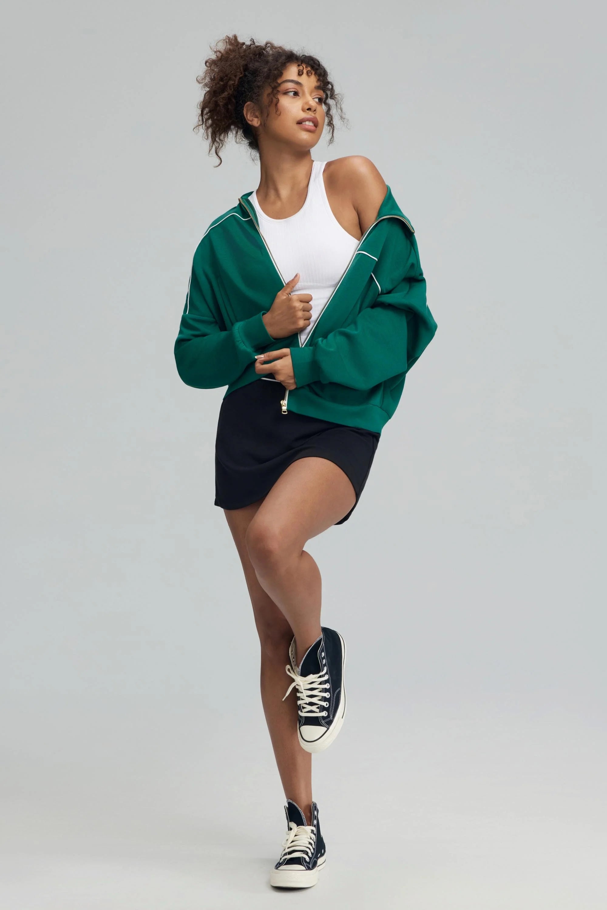 Woman wearing a green cropped golf jacket over a white tank with a mini skirt