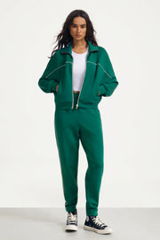 Woman wearing deep teal track pants with a matching jacket and white crop top