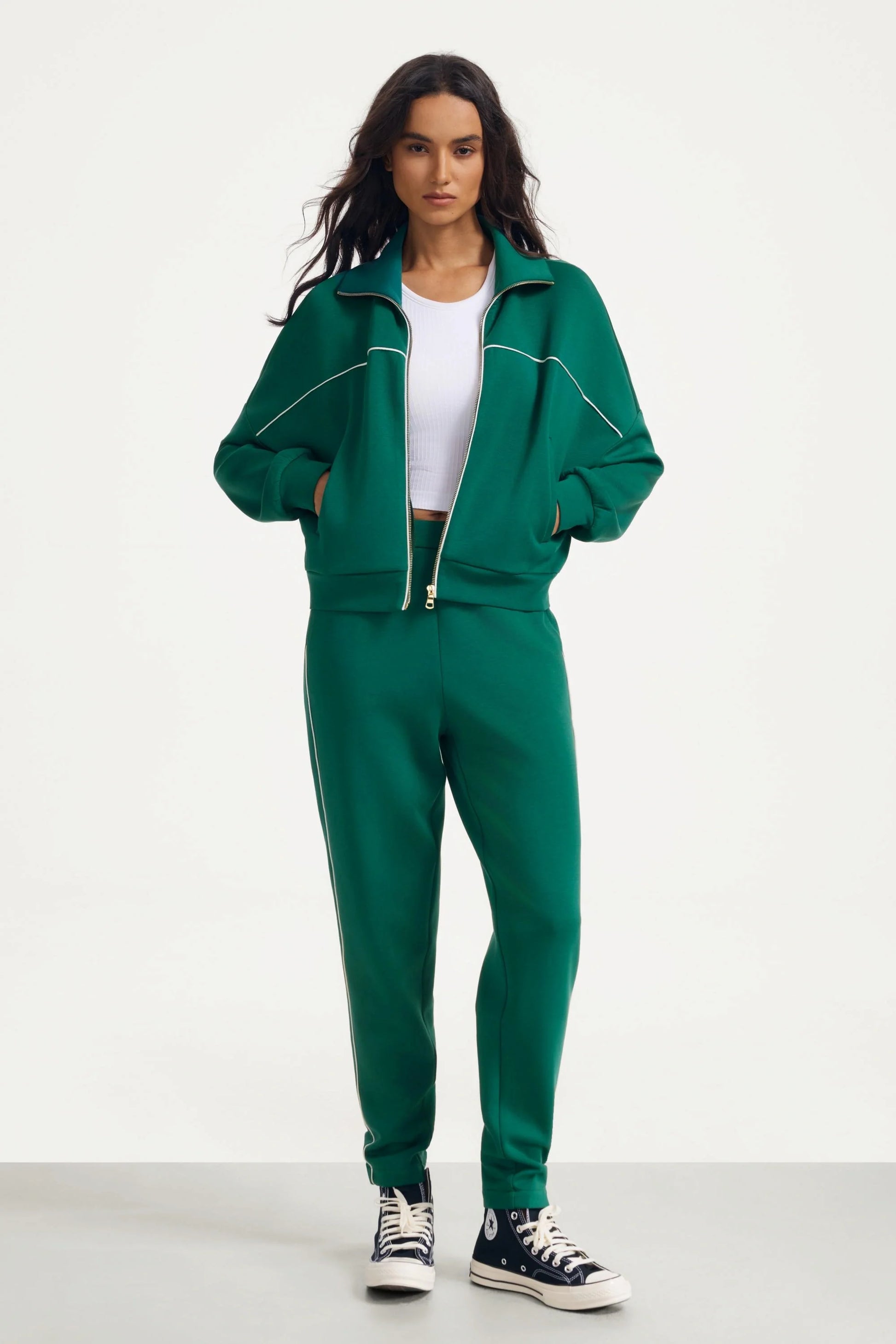 Woman wearing deep teal track pants with a matching jacket and white crop top