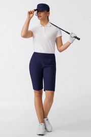Women wearing midnight navy tailored golf shorts styled with a white performance golf polo and visor