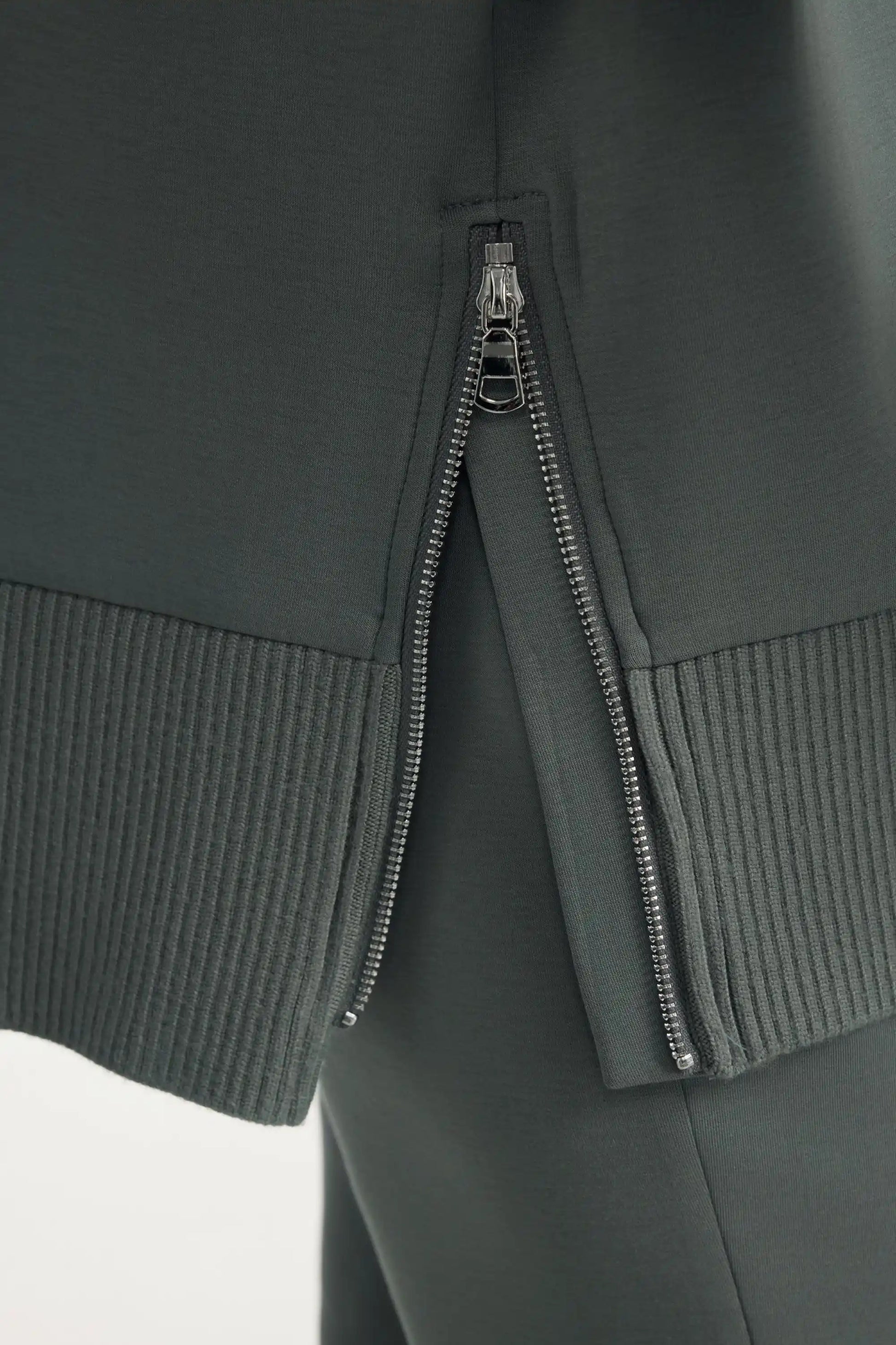 Close-up detail of side zipper and ribbed hem on women’s sage grey funnel-neck pullover
