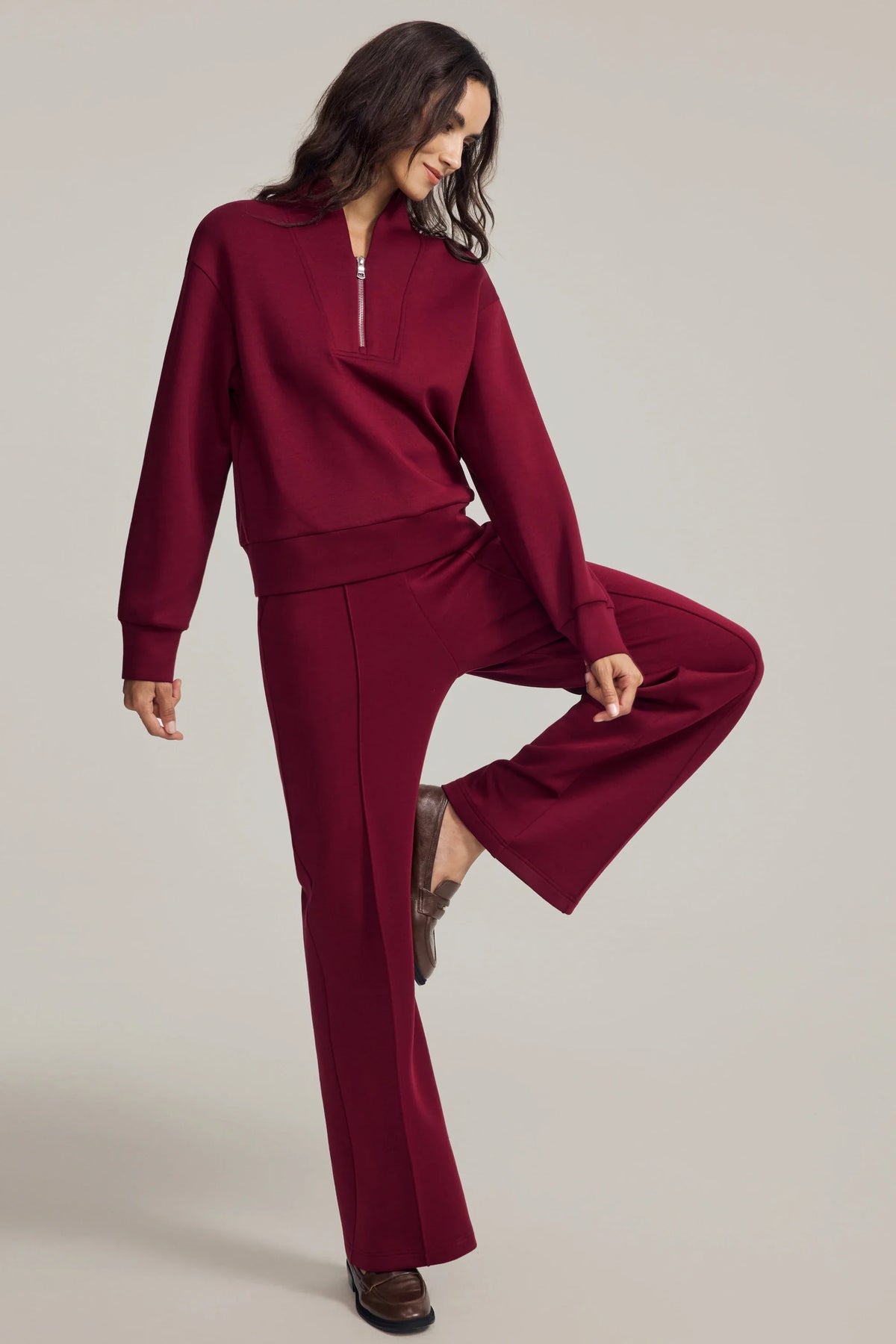 Woman wearing a burgundy half-zip golf pullover and matching straight-leg pants in a raised-leg pose