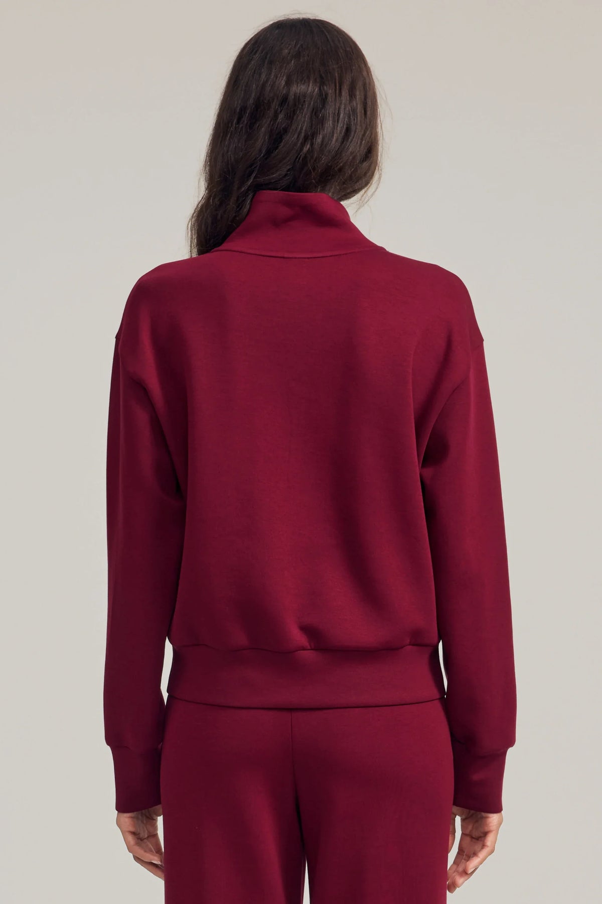 Back view of women's burgundy half-zip golf pullover with dropped shoulders and a clean, relaxed silhouette
