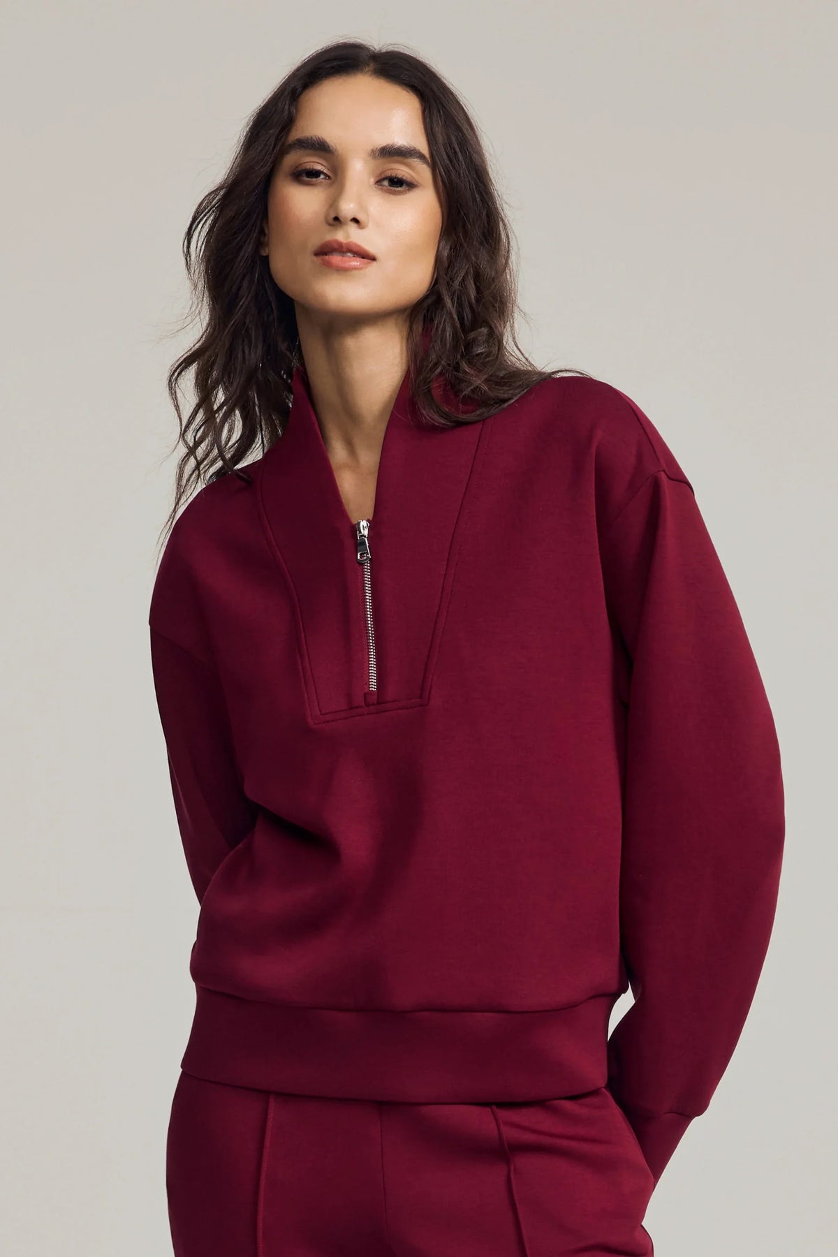 Woman wearing a burgundy half-zip golf pullover with a structured stand collar, relaxed fit and matching pants