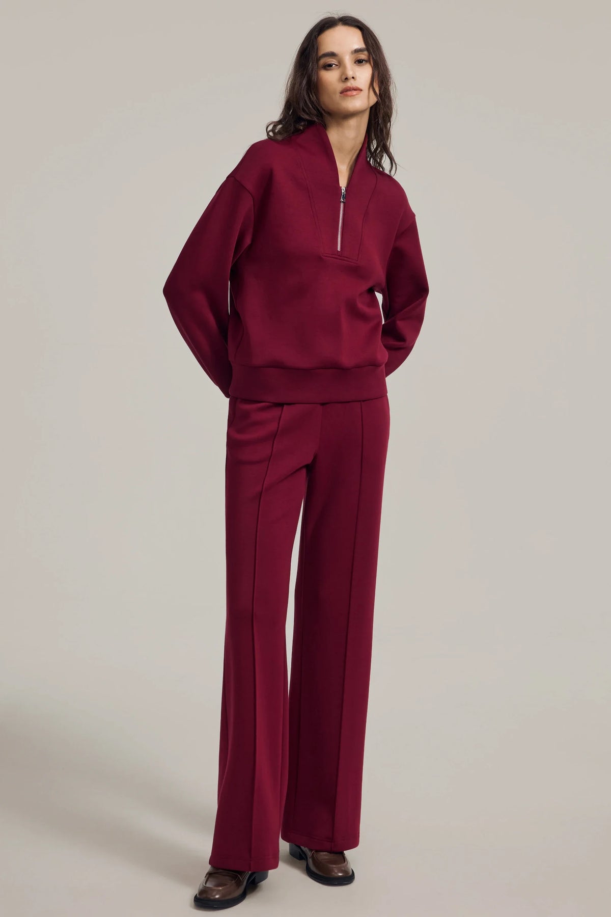 Woman standing with hands on hips in a burgundy half-zip golf pullover and matching pants, showing the relaxed fit