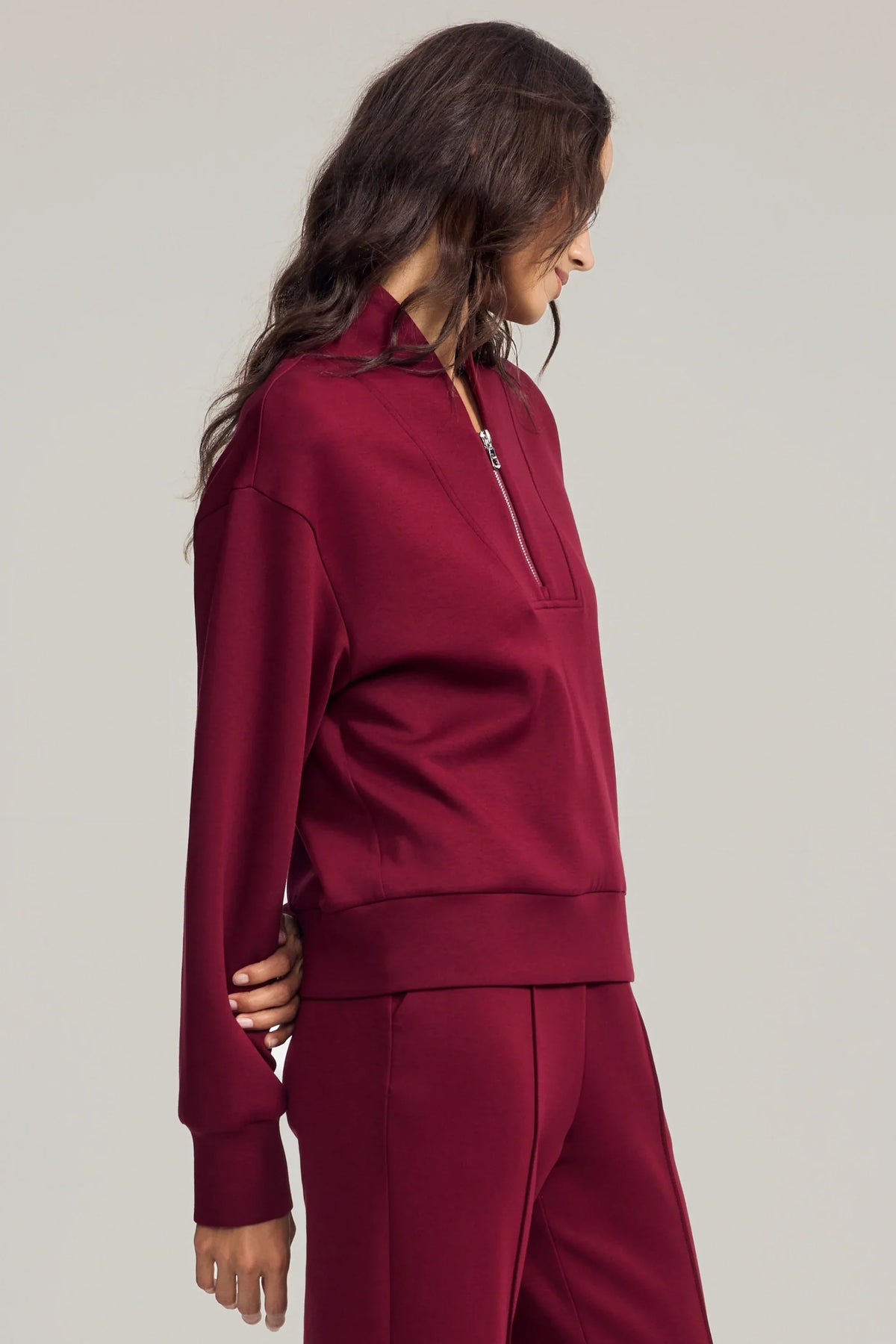 Three-quarter view of women's burgundy half-zip golf pullover showing the relaxed silhouette and dropped shoulders