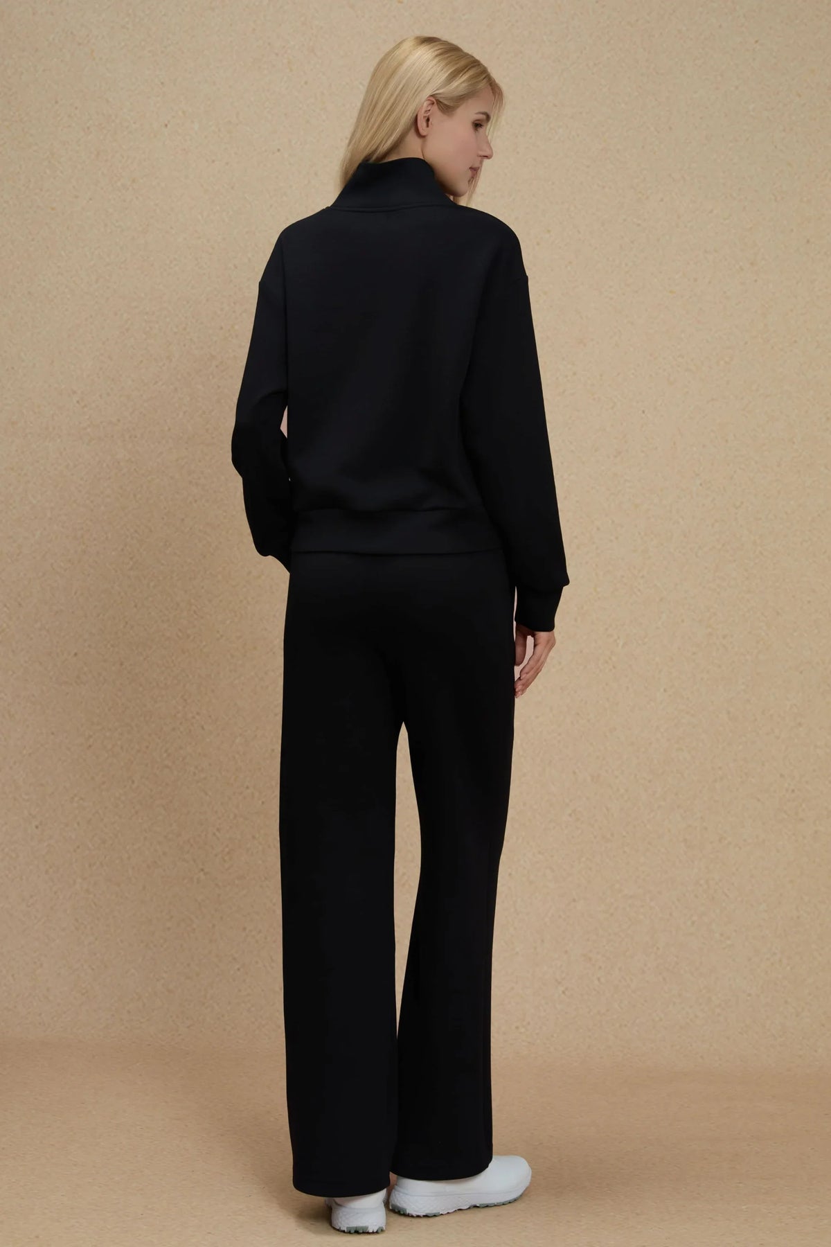 Back view of women's Onyx Black half-zip golf pullover showing the relaxed silhouette, dropped shoulders and matching fabric hem
